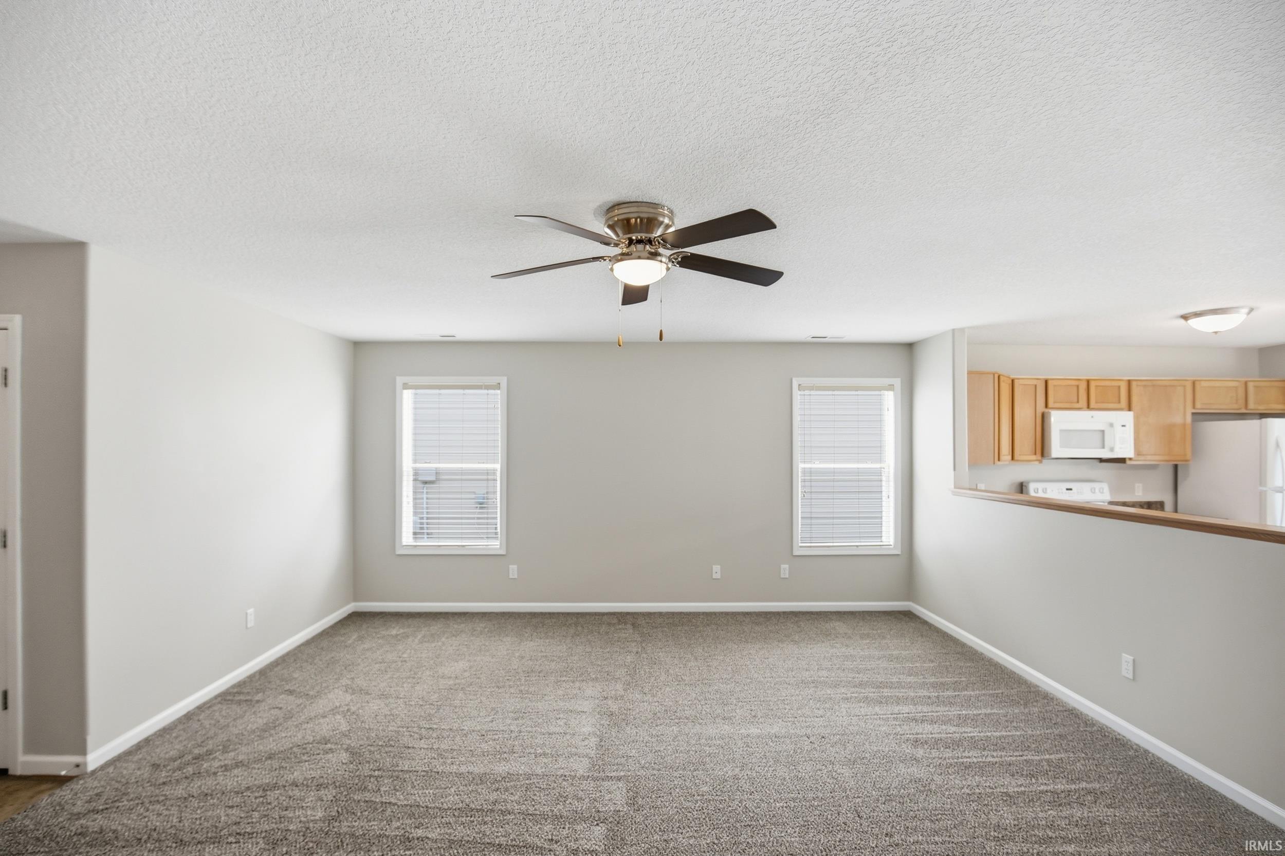 Spacious room featuring neutral carpeting, light gray walls, two windows with blinds, and a bronze-finish ceiling fan