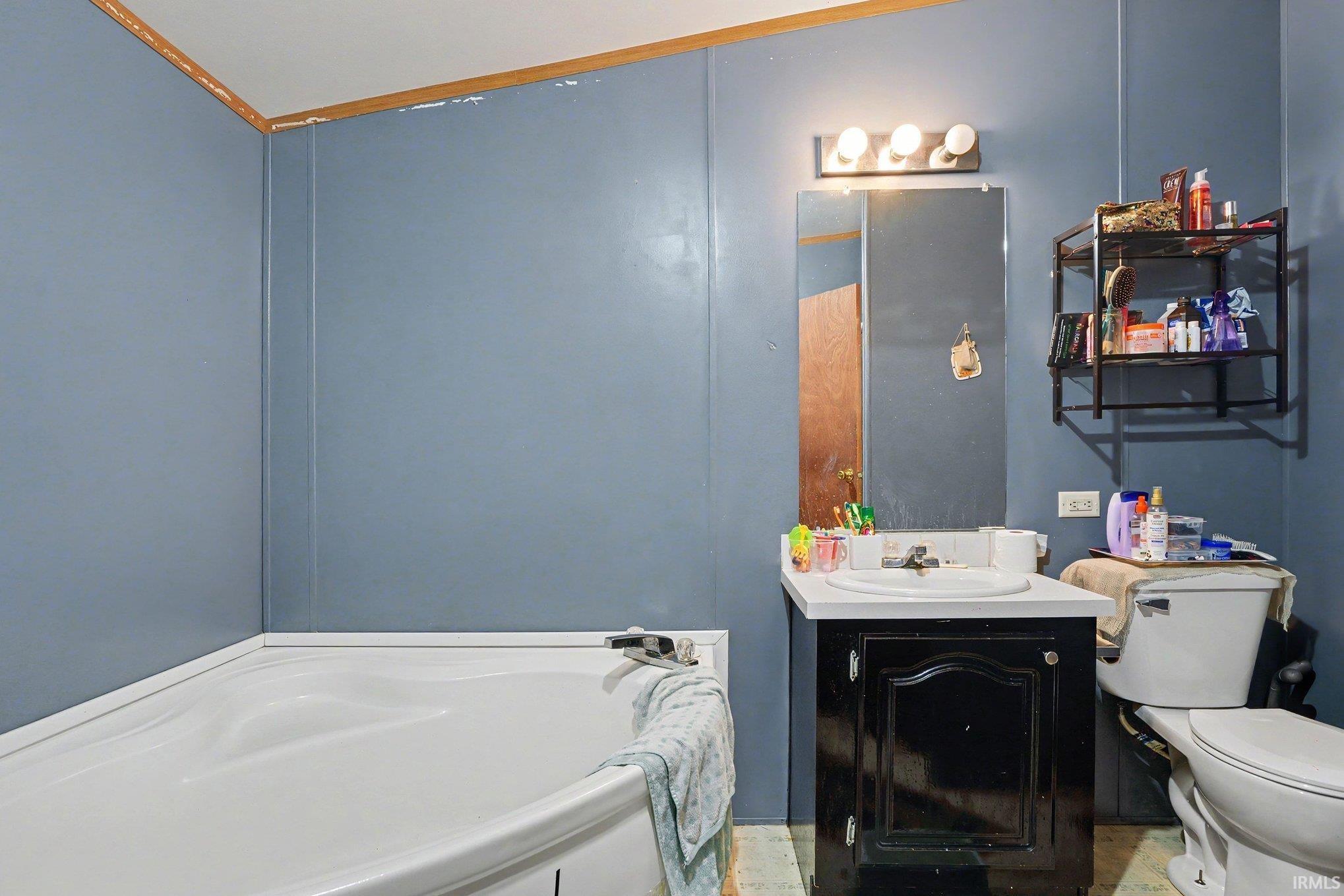 Bathroom featuring a white bathtub, a vanity with an integrated sink, a wall-mounted mirror, a three-light fixture, and blue wall paneling
