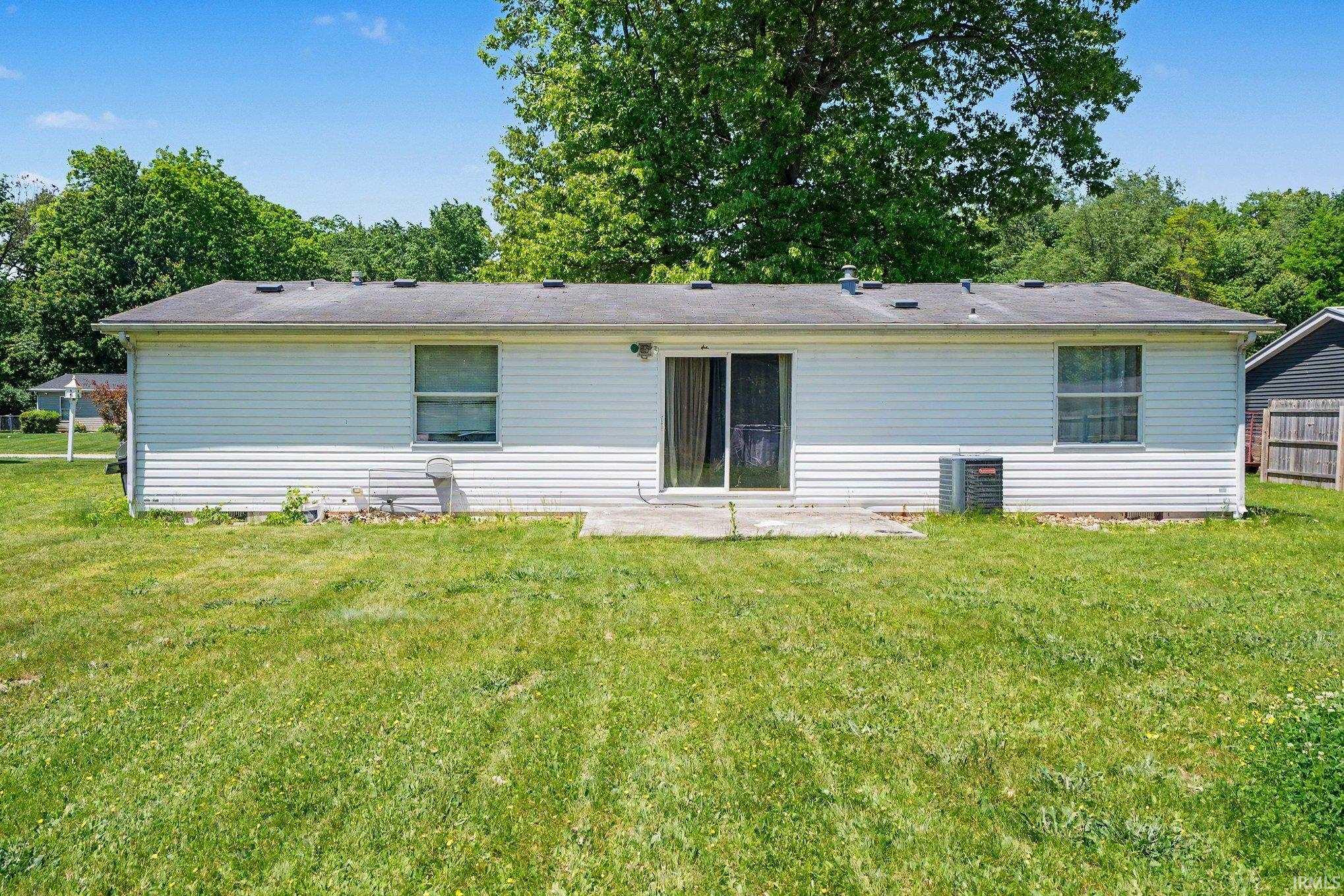 Rear exterior featuring white horizontal siding, a flat concrete patio, sliding glass doors, and a central HVAC unit
