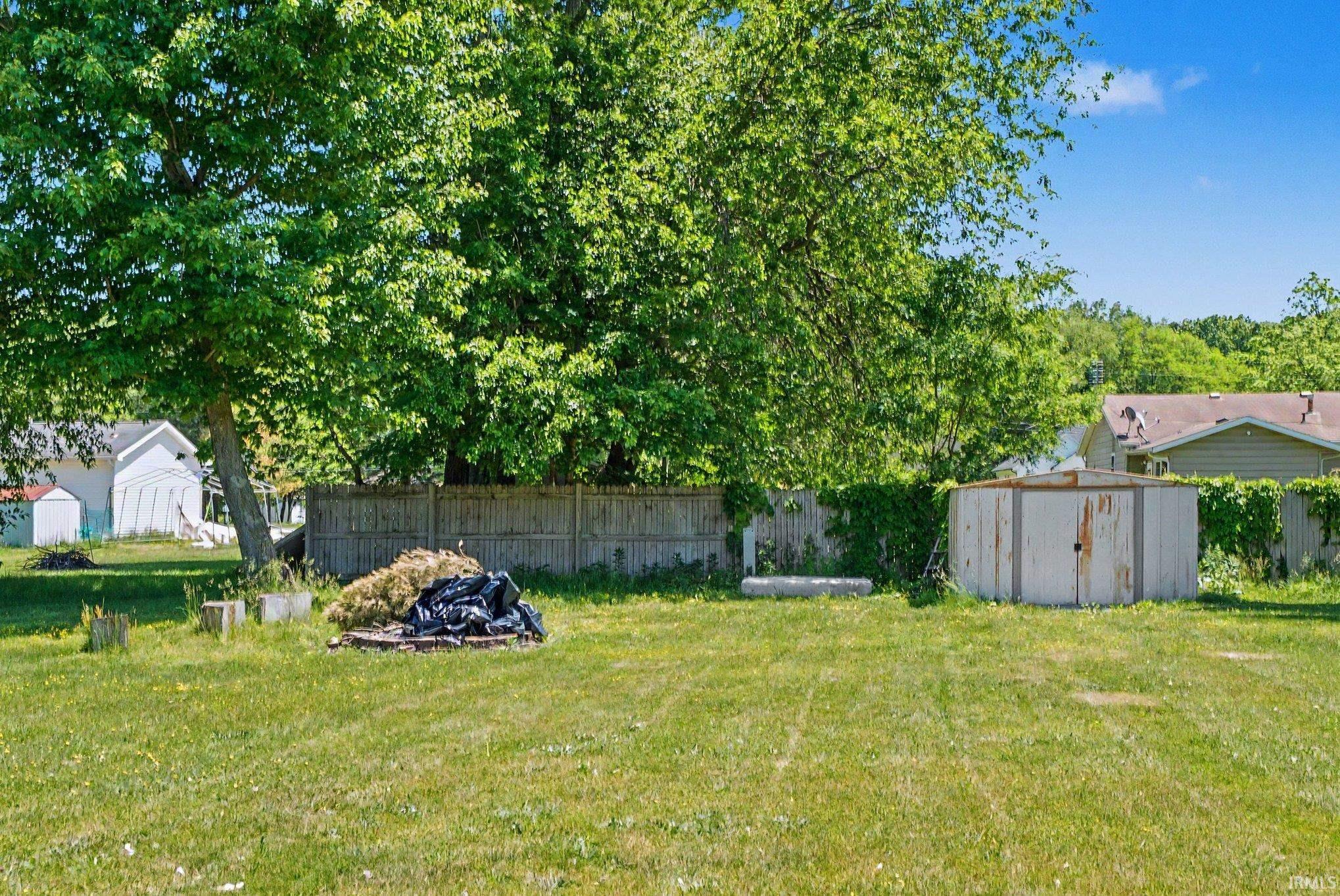 Expansive grassy yard area featuring mature trees, a wooden perimeter fence, and a storage shed