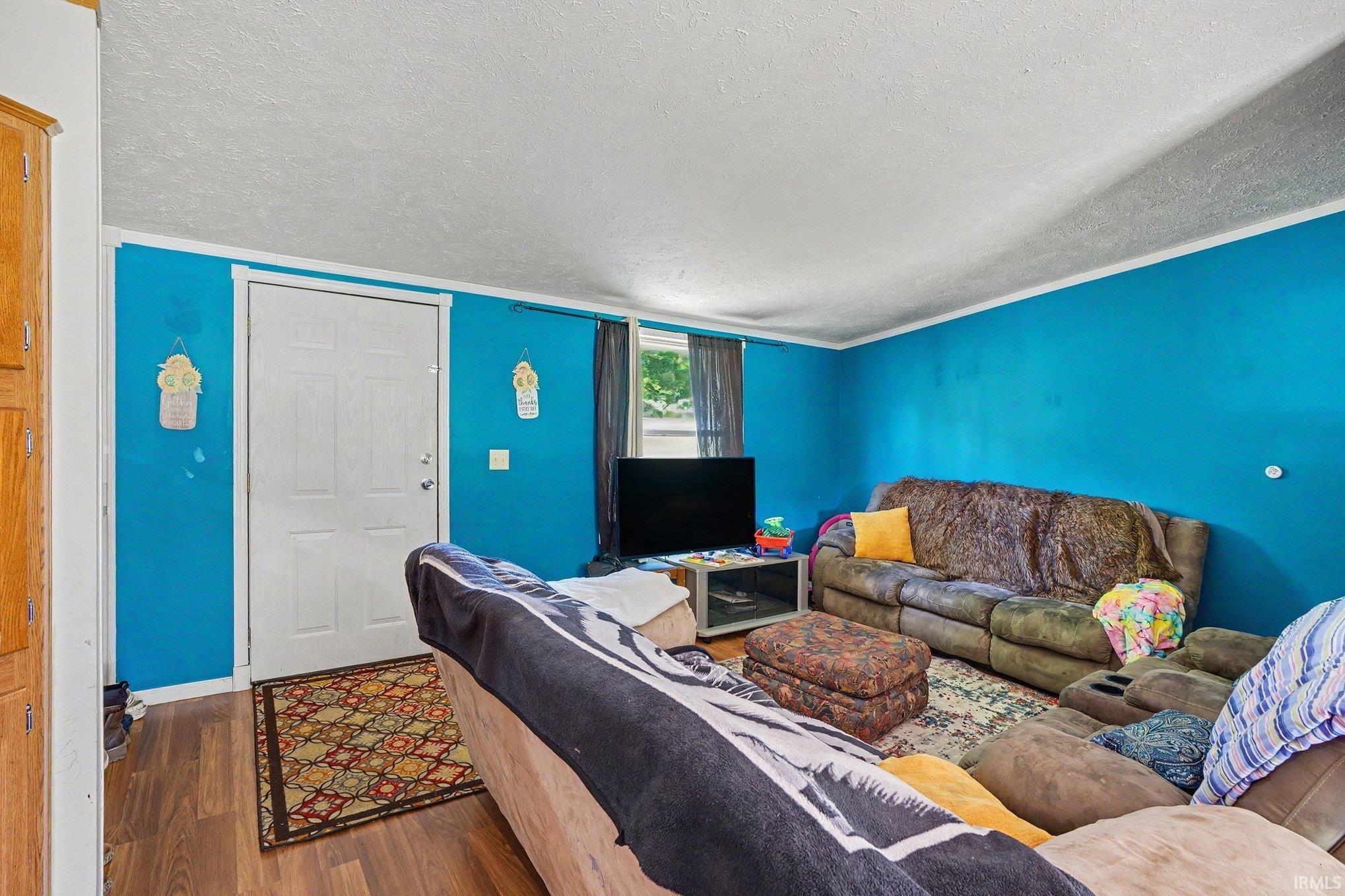 Living area featuring wood-finish flooring, a white paneled door with white trim, and a window with dark drapes
