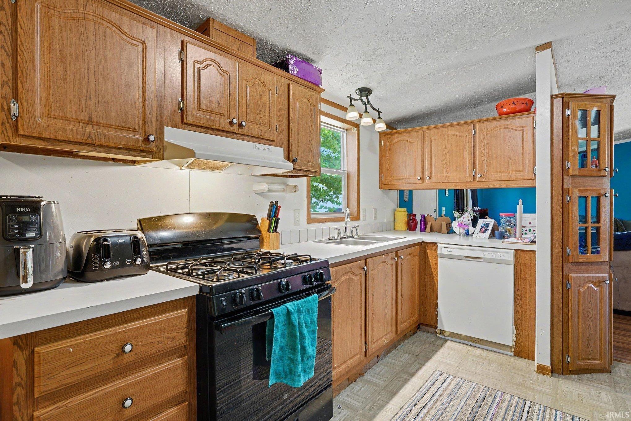 Kitchen featuring wood-finish cabinetry, white countertops, and a full suite of appliances including a black range and white dishwasher