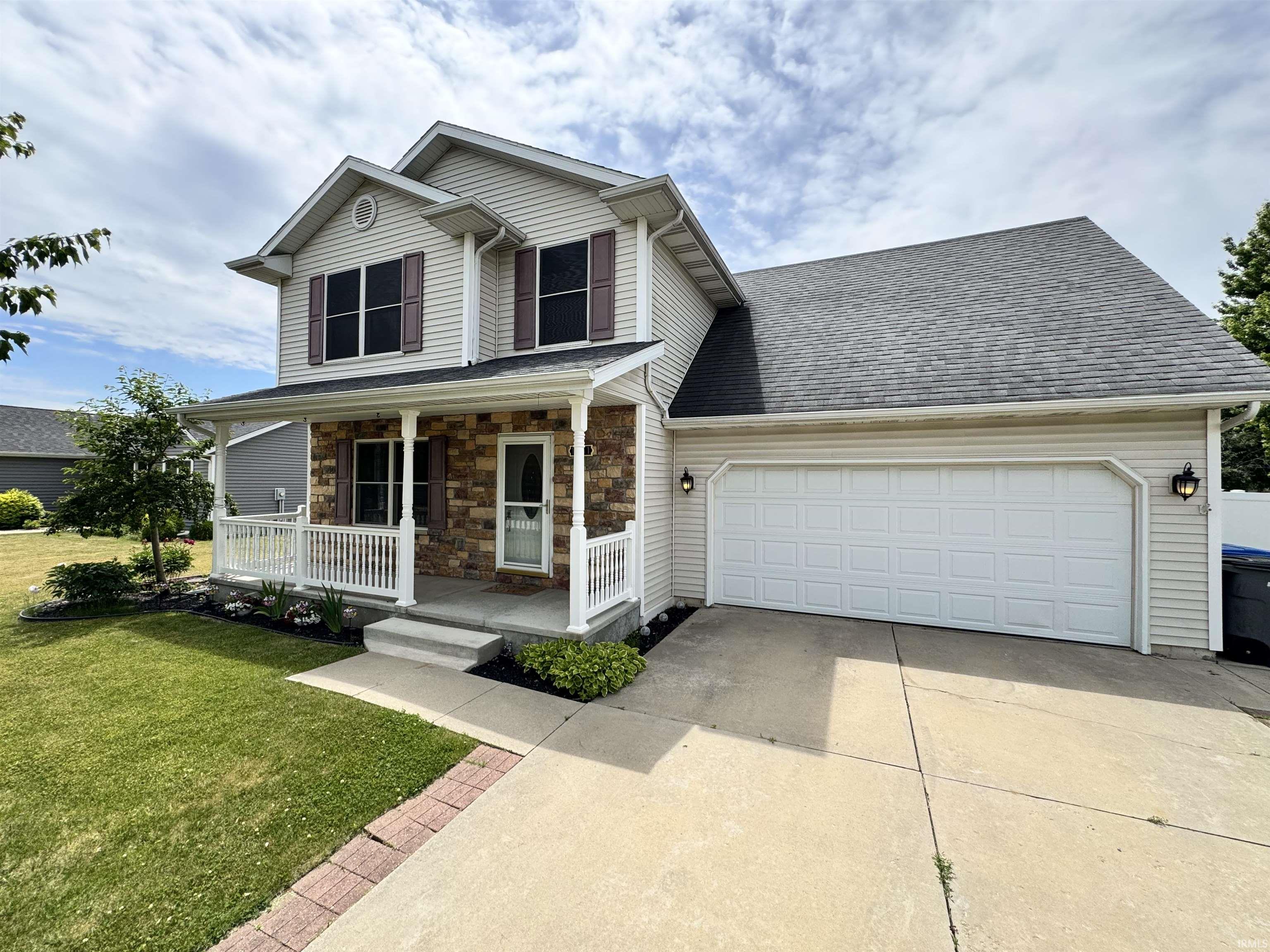 Two-story residence featuring a covered front porch with white railing, stone accents on the facade, and a two-car garage