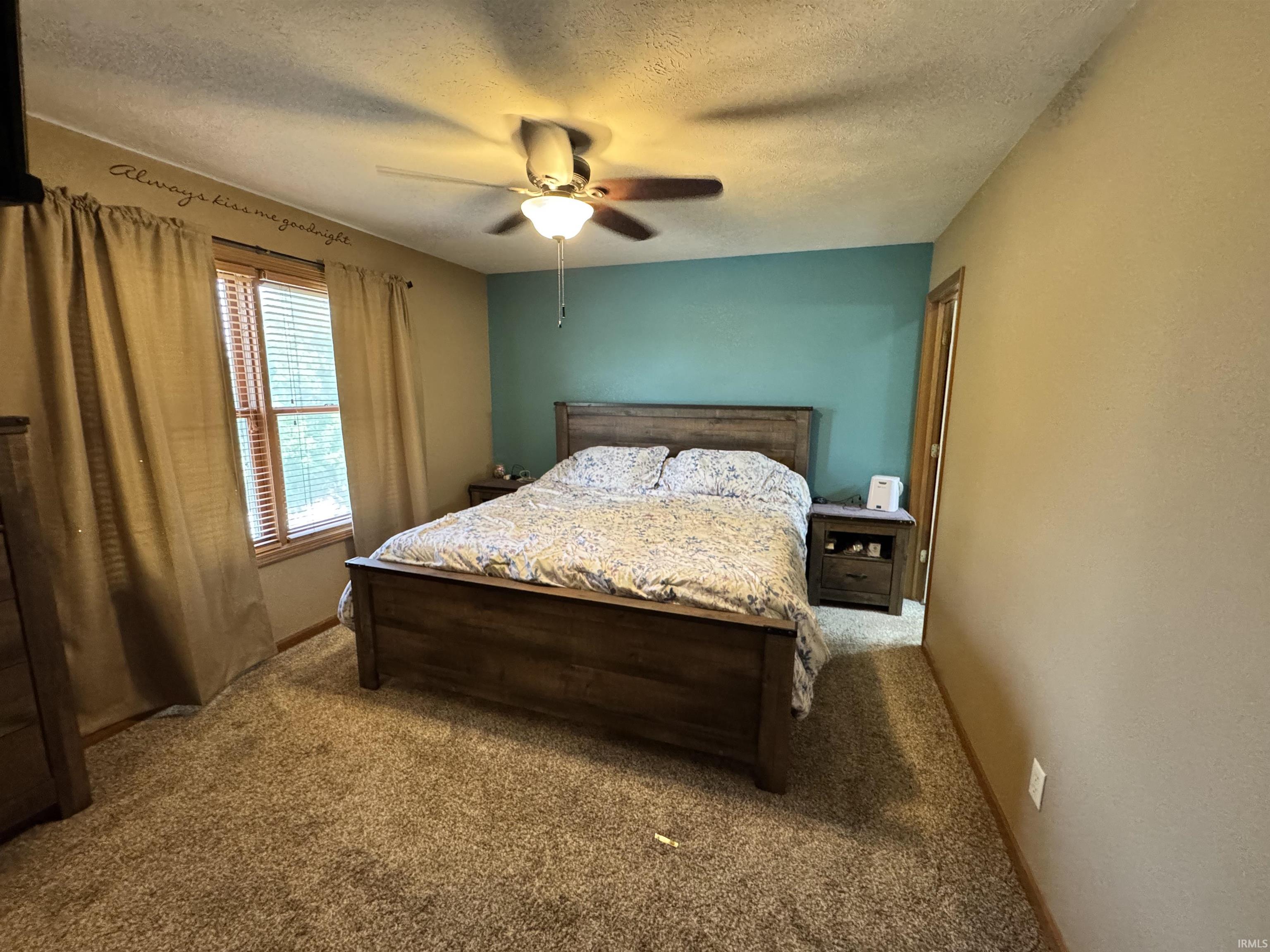 Carpeted bedroom featuring a ceiling fan with integrated lighting, a contrasting accent wall, and a window with blinds