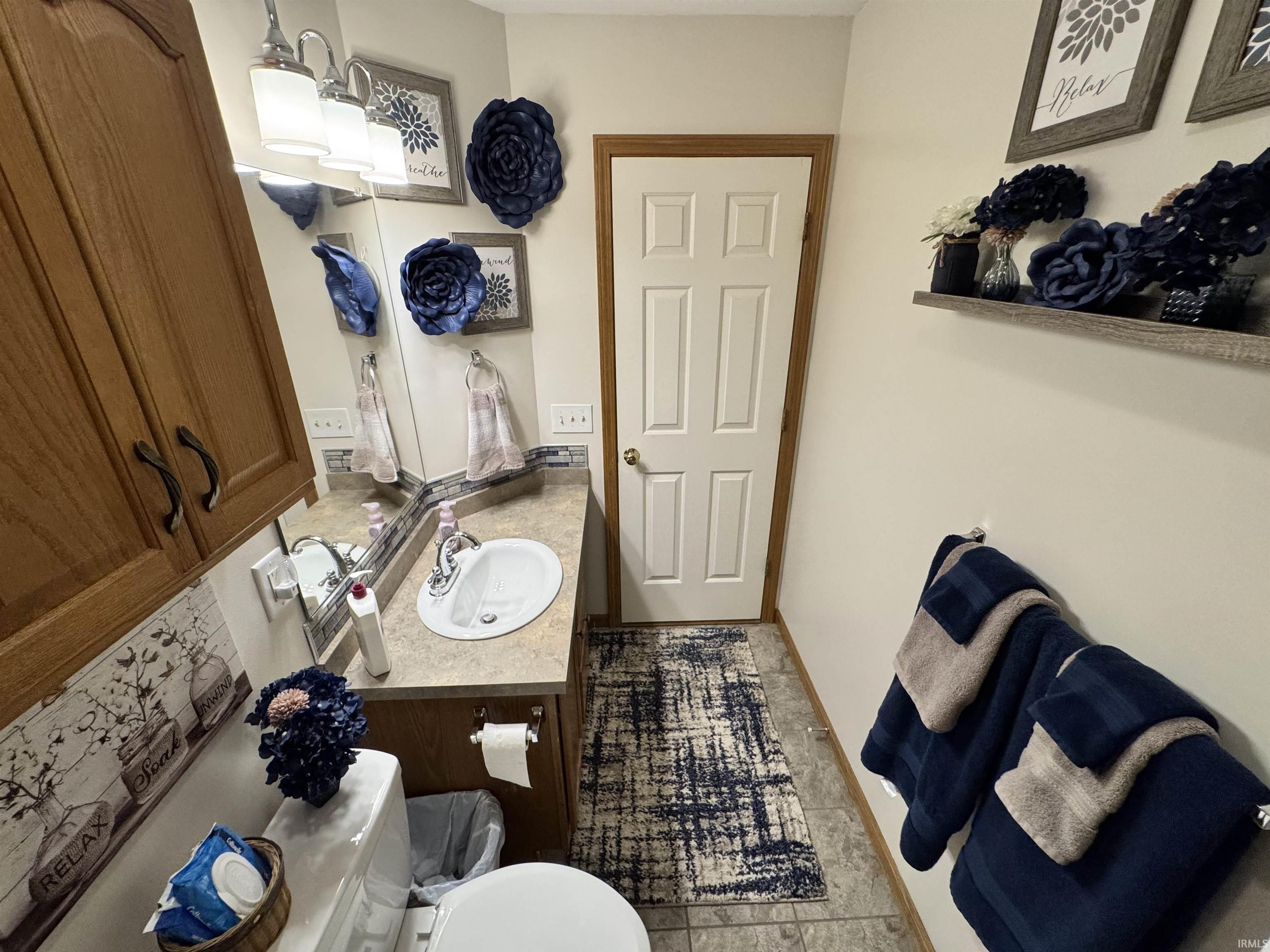 Bathroom featuring a single vanity with a laminate countertop, a white porcelain sink, and a mirrored wall