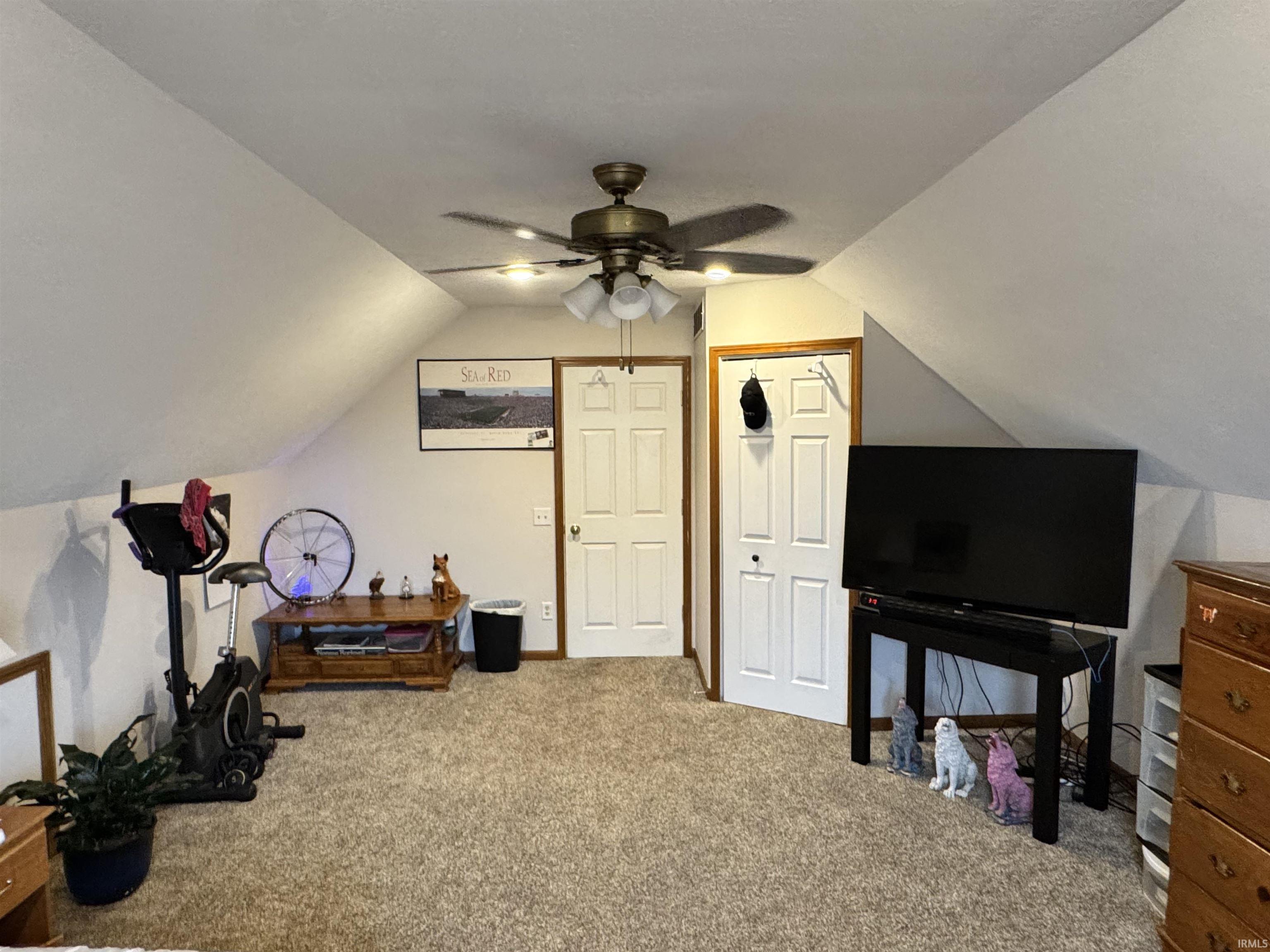 Carpeted room with sloped ceilings and a ceiling fan with integrated lighting