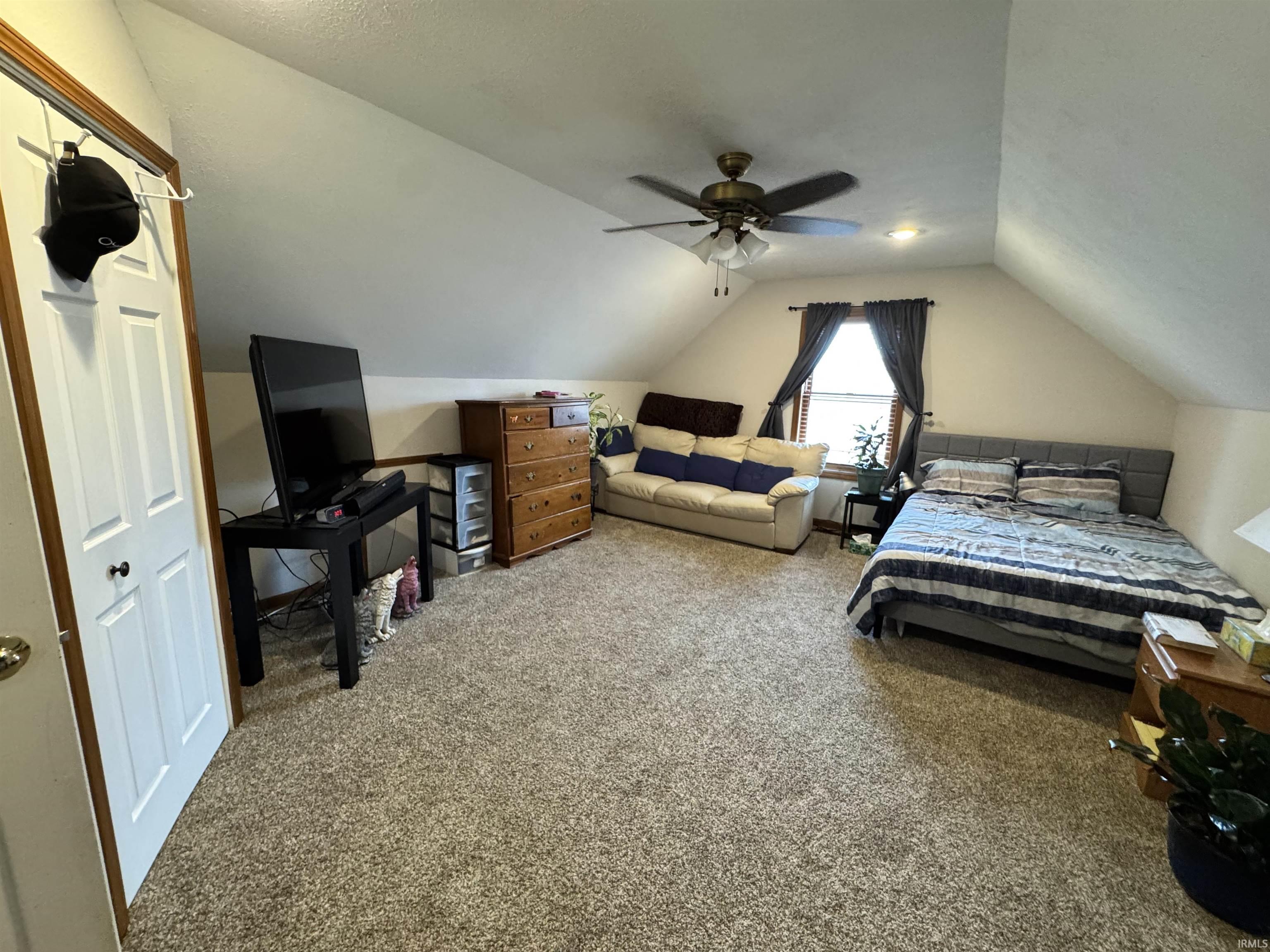 Carpeted room featuring a ceiling fan, sloped ceilings, and a window with curtains
