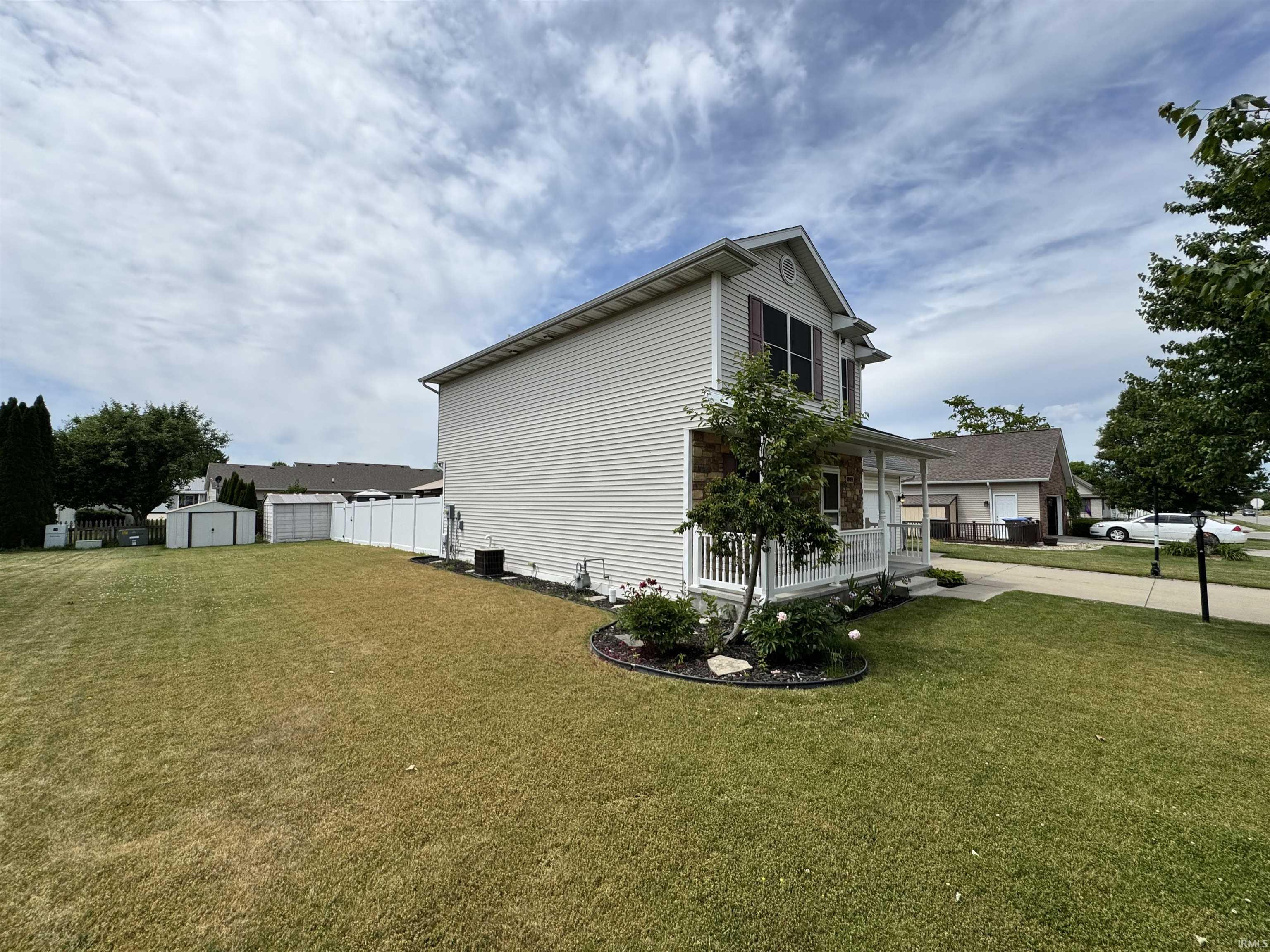 Two-story residence featuring light-colored siding, a covered front porch with white railings, and decorative stone accents