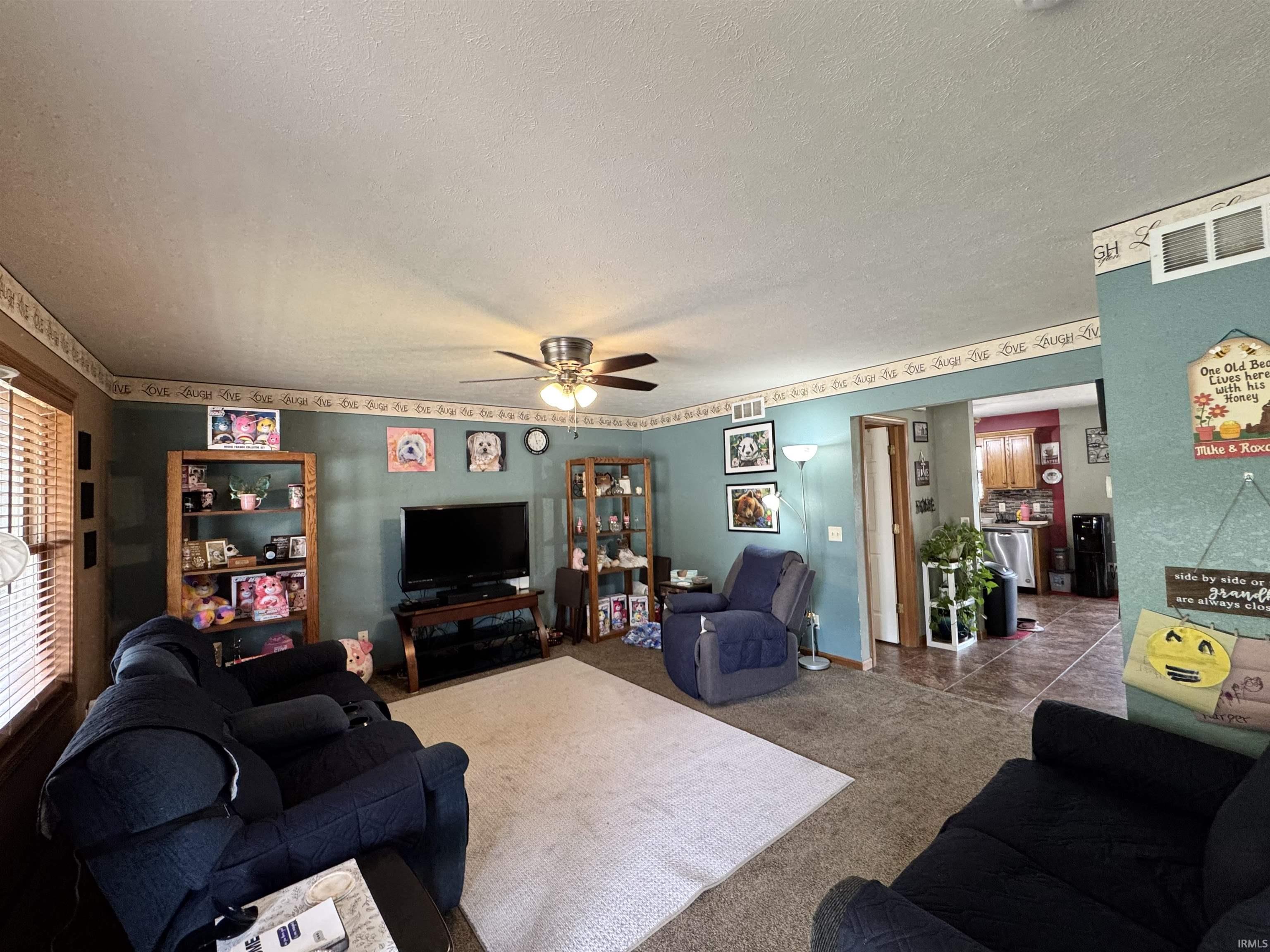 Carpeted living area featuring a ceiling fan with light fixture, a window with horizontal blinds, and built-in shelving