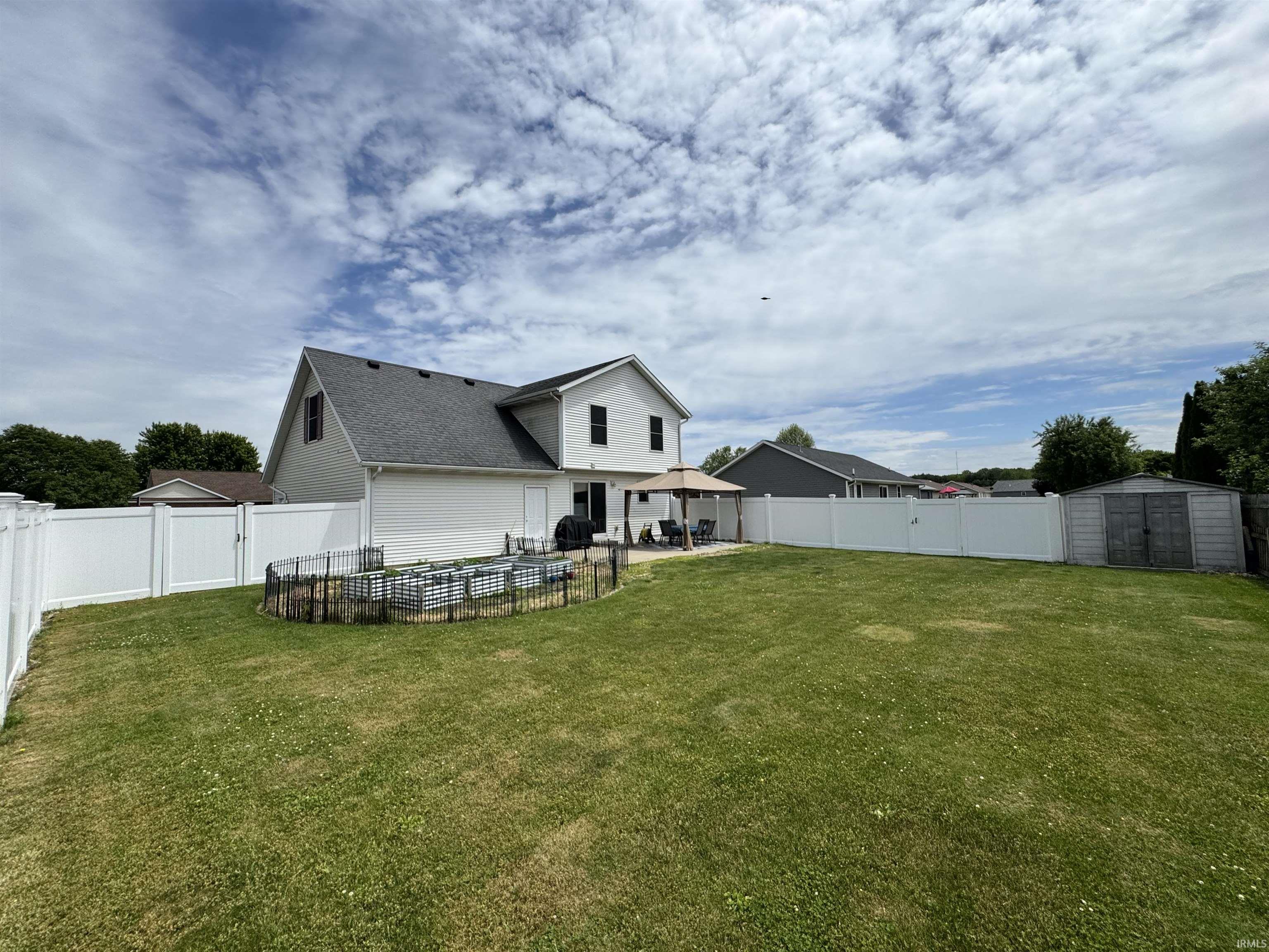 Expansive backyard featuring a white vinyl privacy fence, a concrete patio, and an outdoor shed