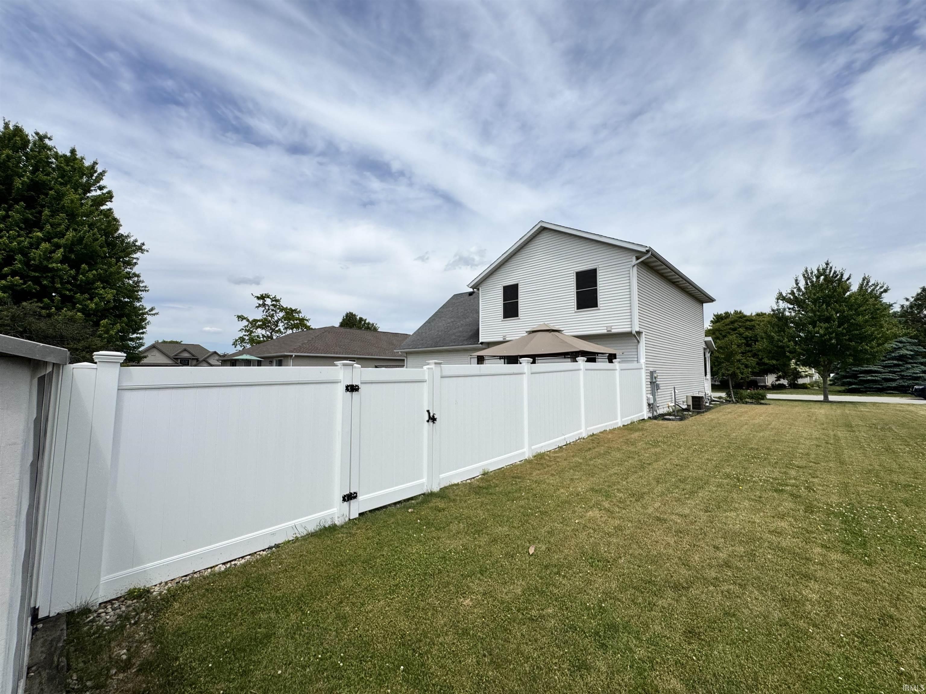 Expansive backyard featuring a manicured lawn, white vinyl privacy fence, and multiple privacy gates
