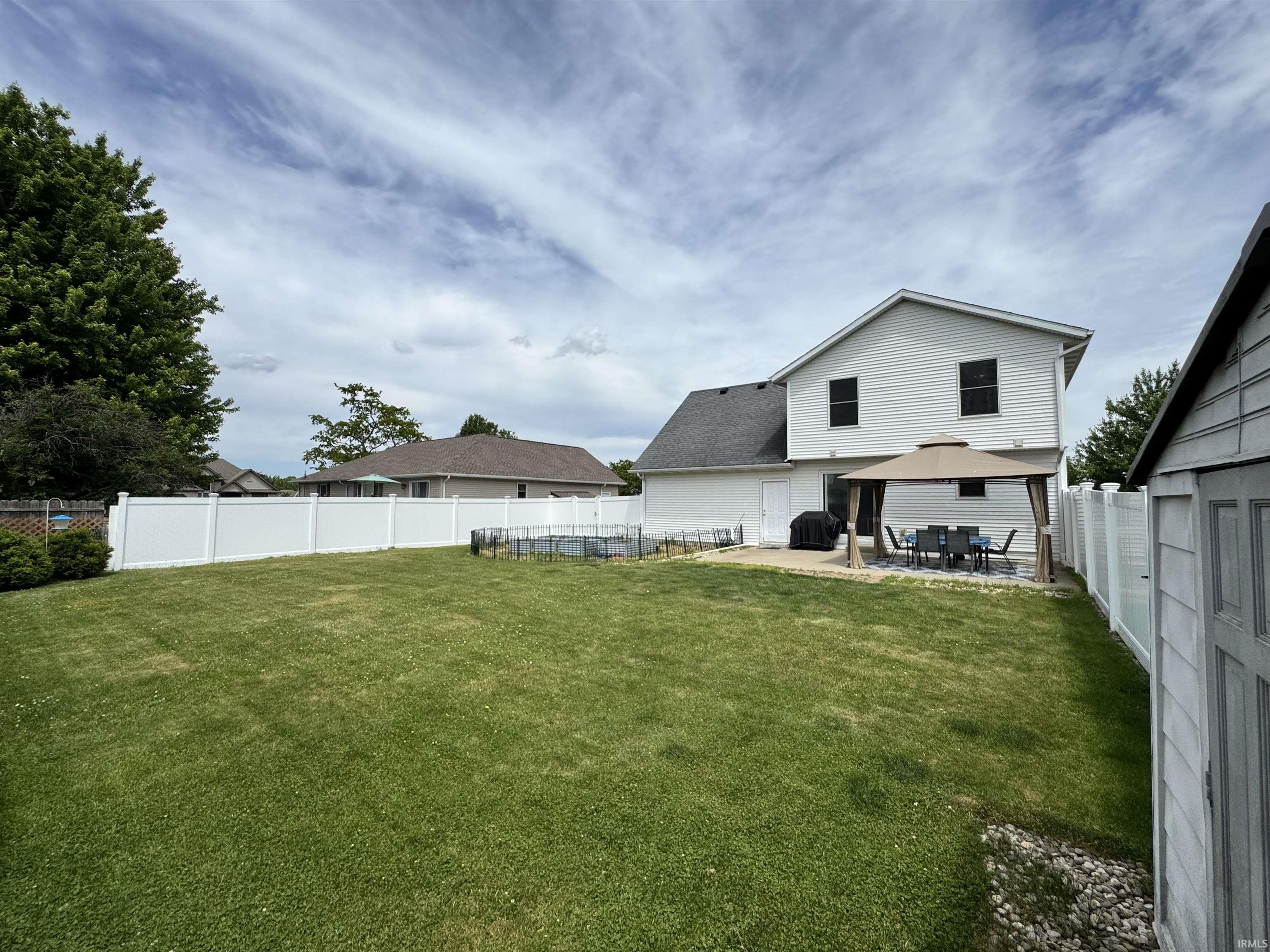 Expansive backyard featuring a manicured lawn, a full white vinyl privacy fence, a concrete patio, and a separate storage shed with vinyl siding