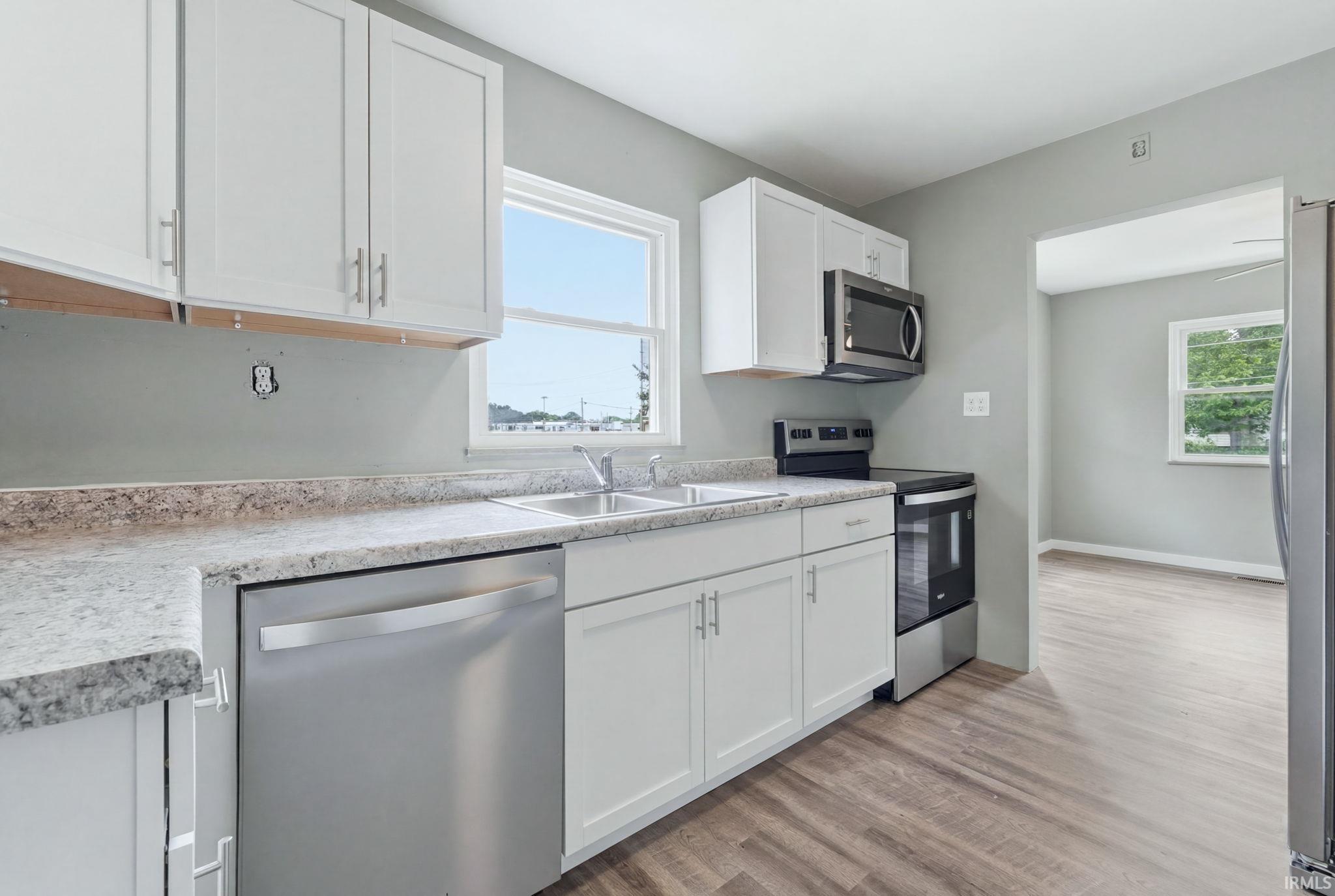 Kitchen featuring white shaker cabinetry, light-toned countertops, stainless steel appliances, and wood-finish flooring