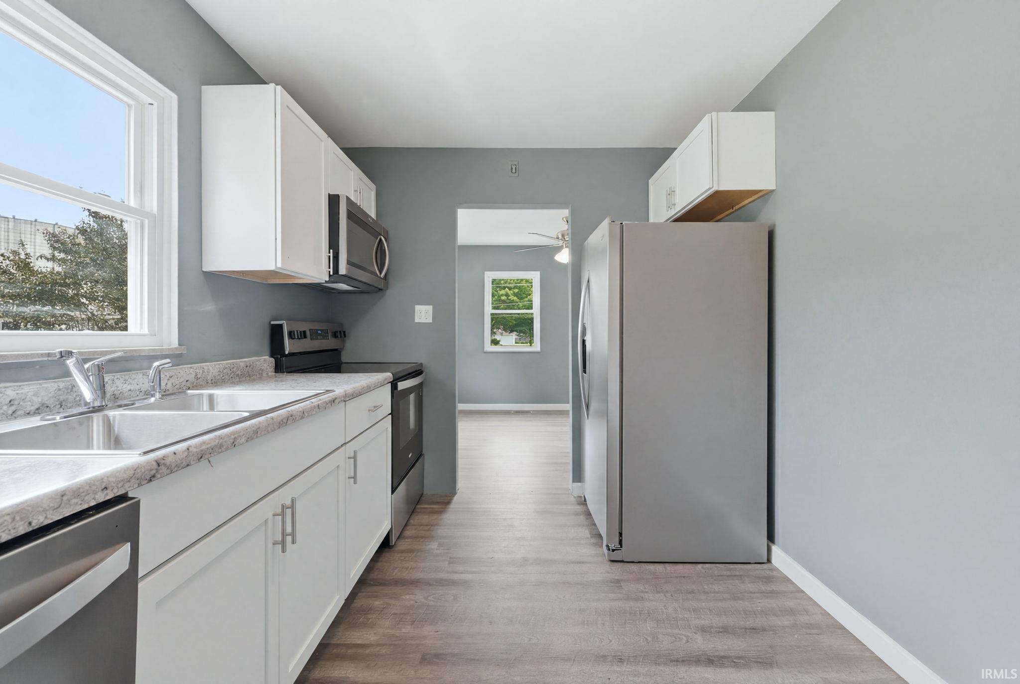 Modern kitchen featuring white cabinetry, light-colored countertops, stainless steel appliances, and wood-finish flooring