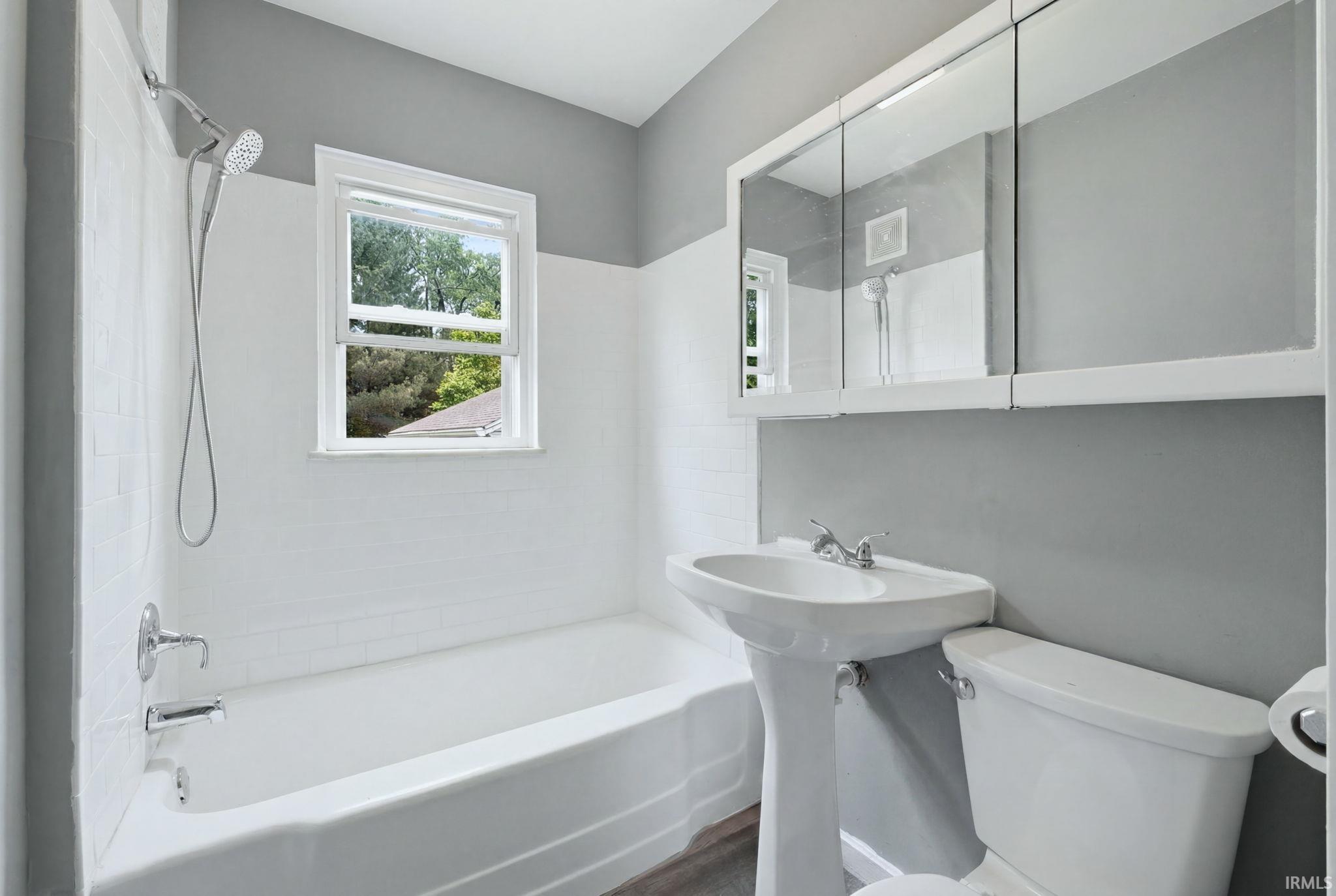 Bathroom featuring a pedestal sink, white subway tile shower surround, chrome fixtures, and a multi-pane window