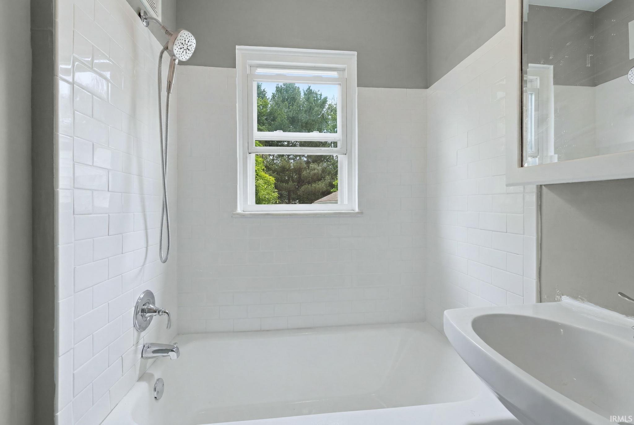 Bathtub with white subway tile surround, chrome shower fixtures, and a window