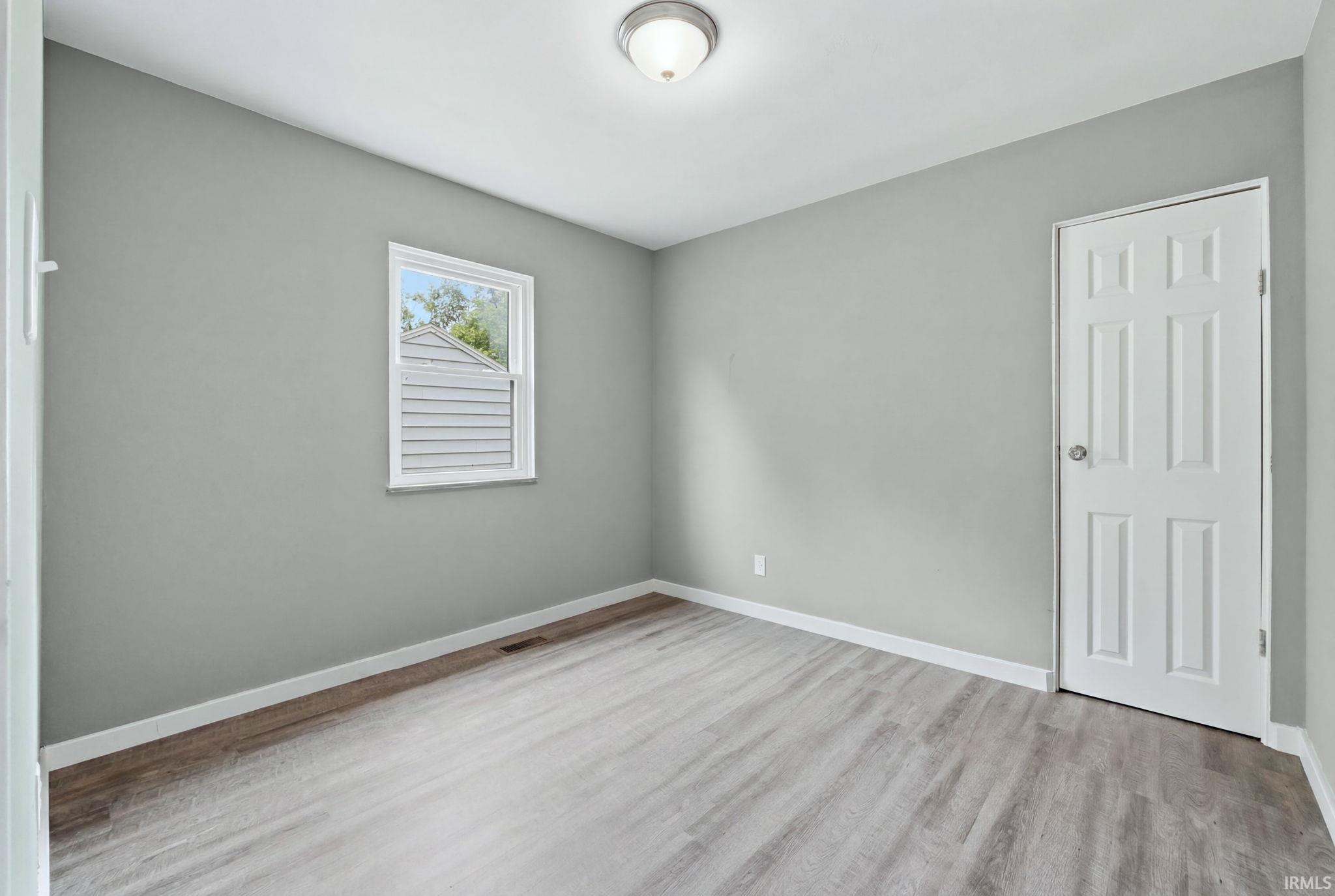 Neutral gray wall paint, wood-finish flooring, white baseboards, and a six-panel interior door