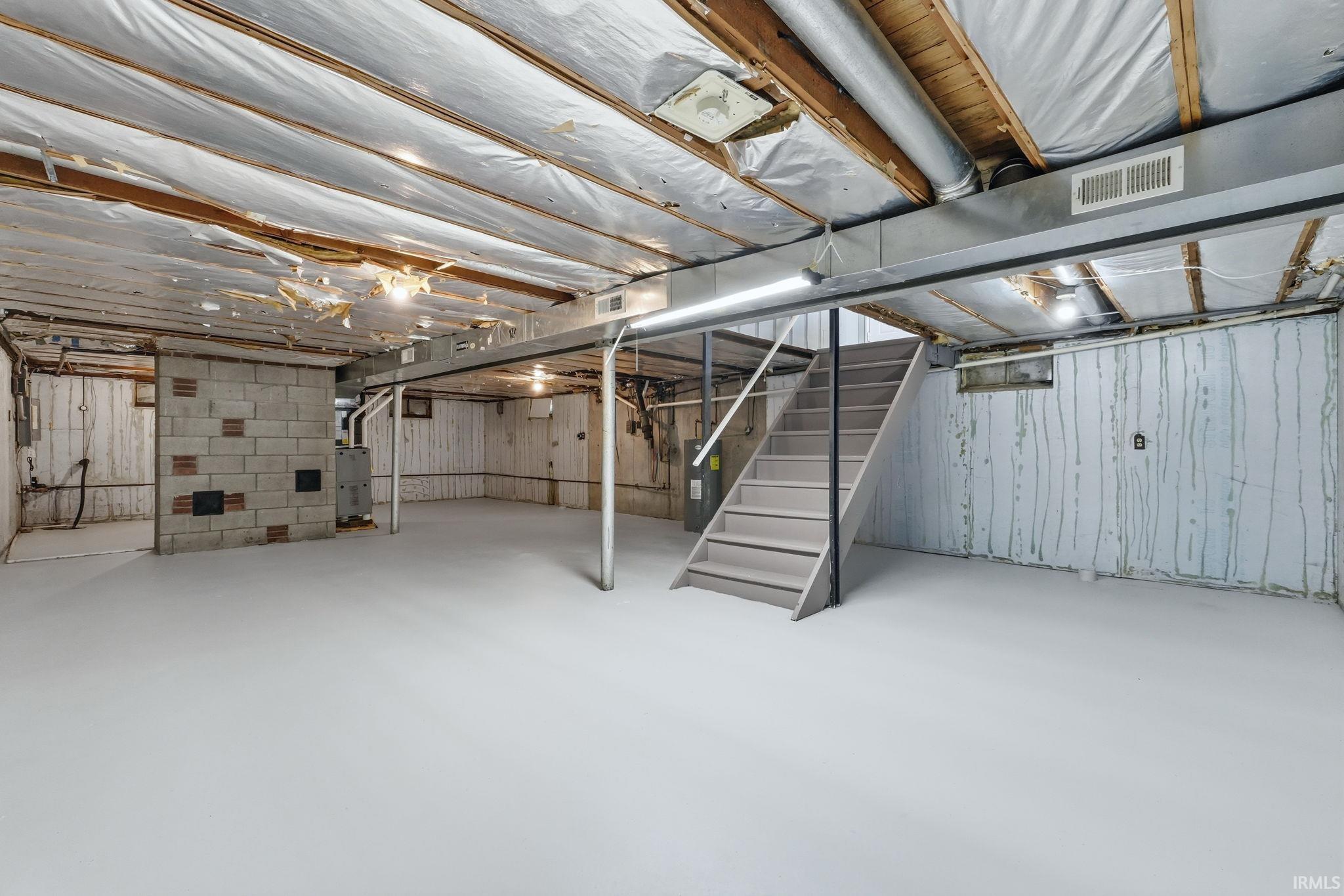 Spacious unfinished basement with painted concrete flooring, exposed ceiling joists, utility sink, and cinder block walls