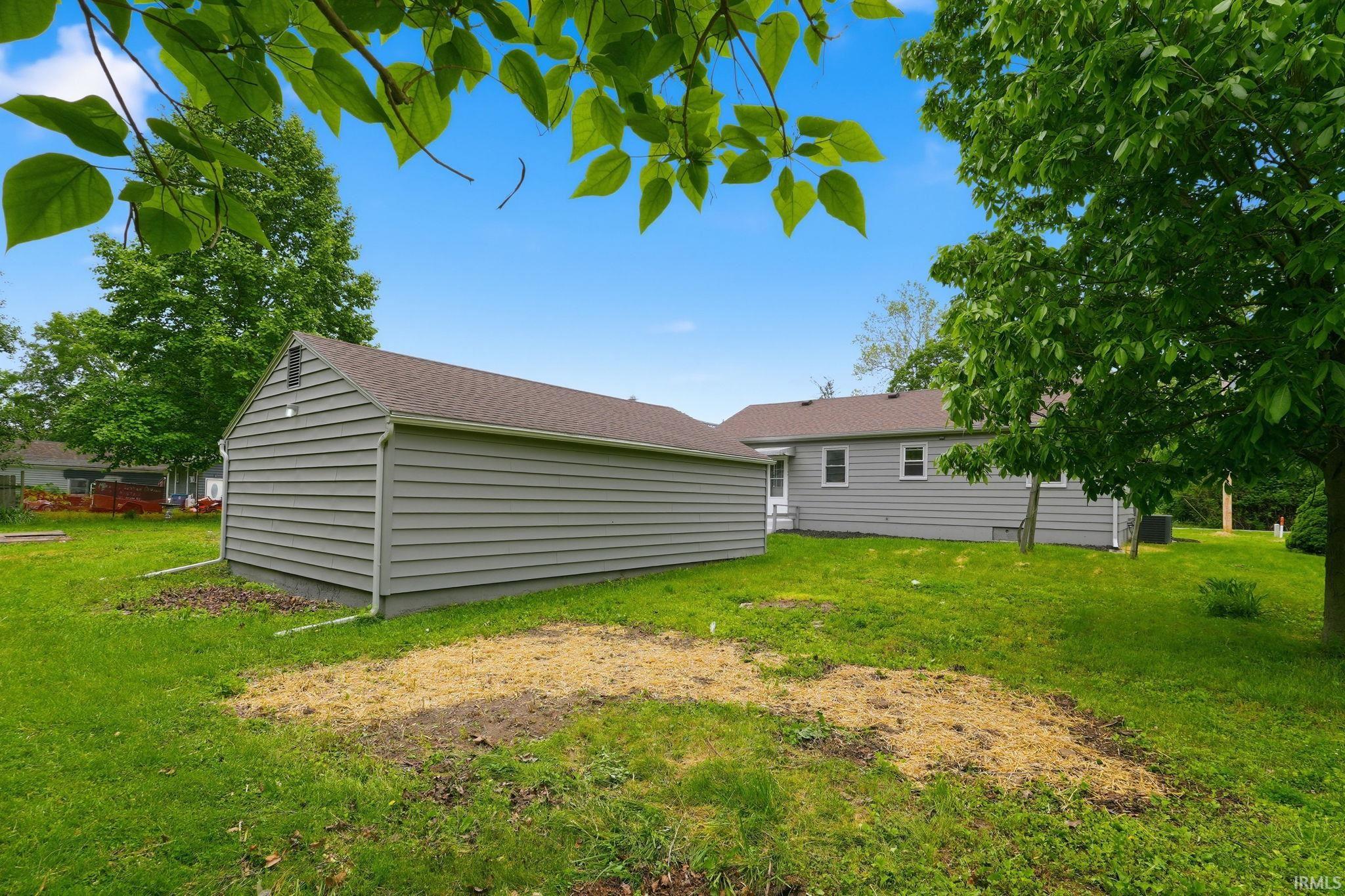 Expansive rear yard featuring green lawn, mature trees, and a detached structure with gray horizontal siding and a brown shingle roof