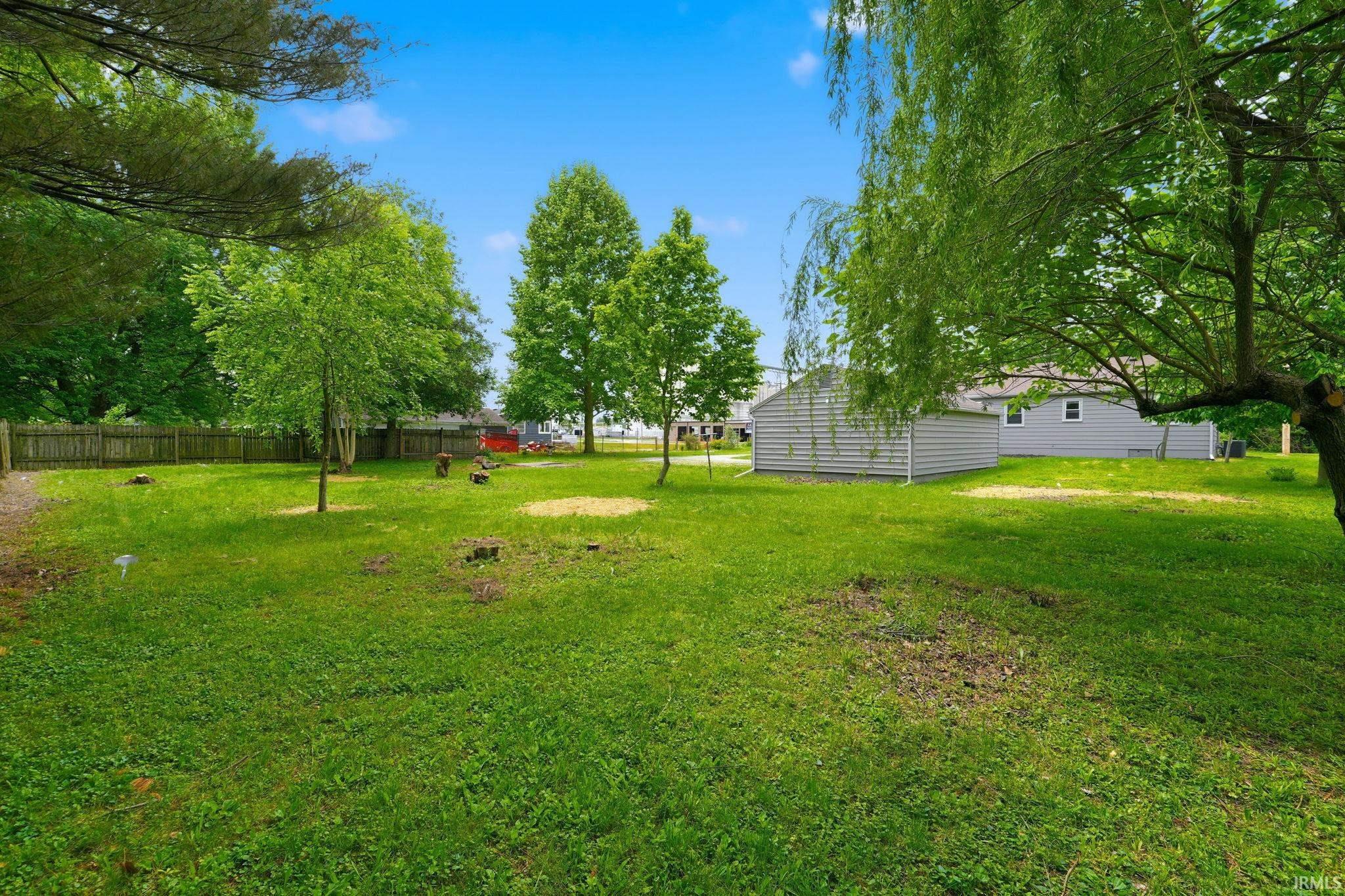 Expansive green yard with mature trees and a wood fence border