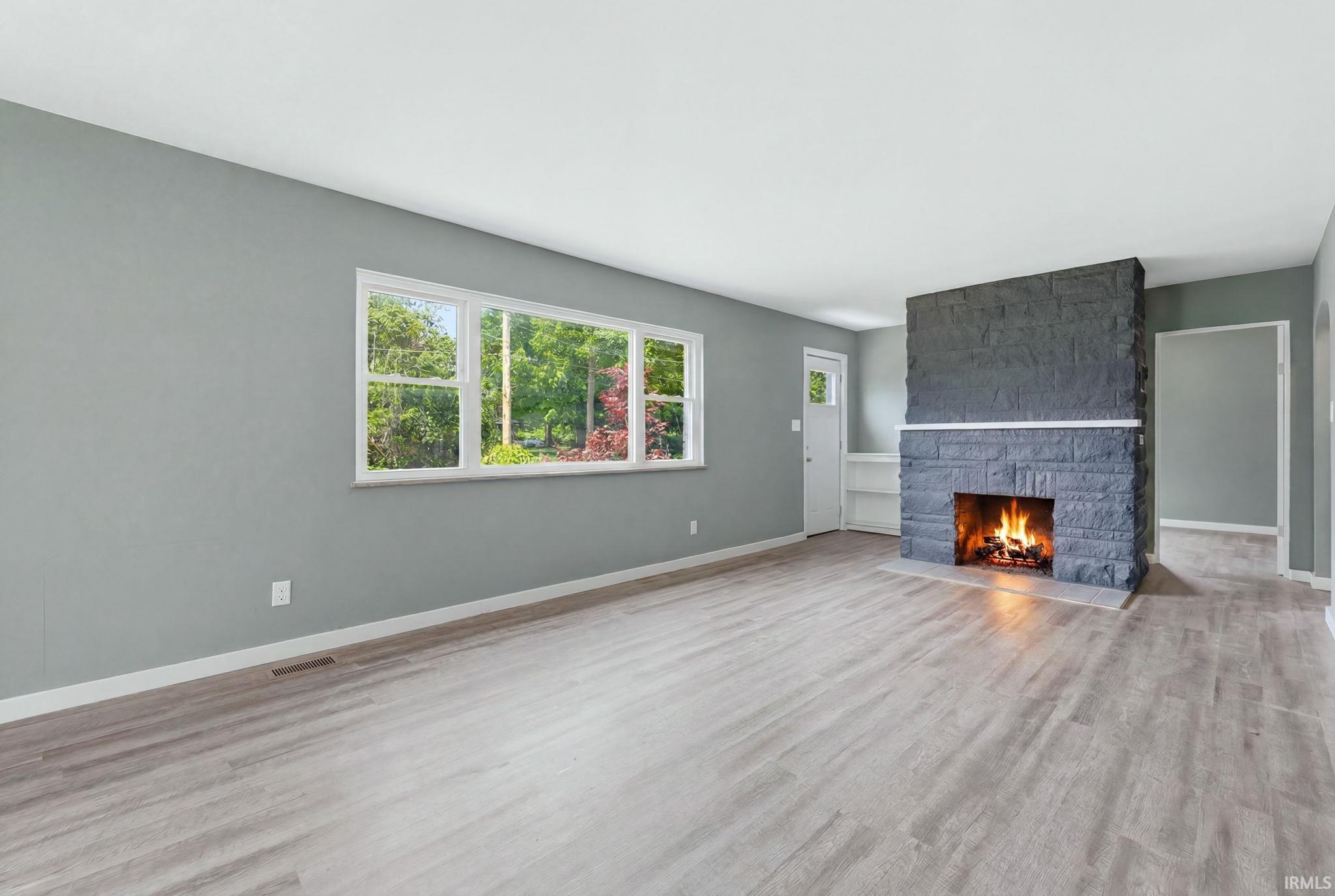 Spacious room featuring a stone fireplace with a contrasting mantel, wood-finish flooring, and a large window