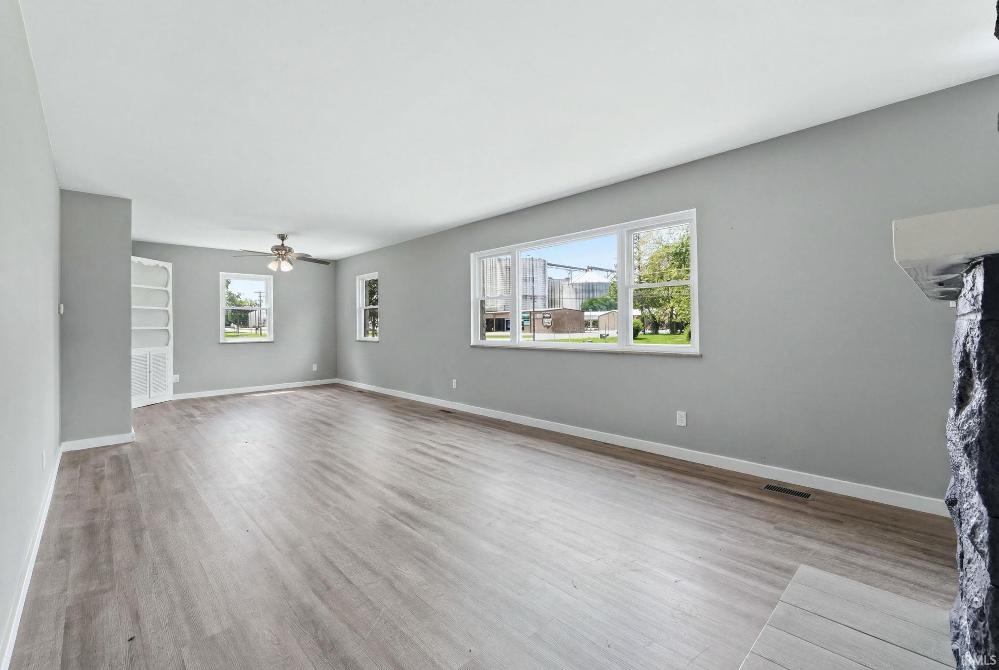 Spacious room featuring wood-finish flooring, light grey walls, white trim, and multiple windows