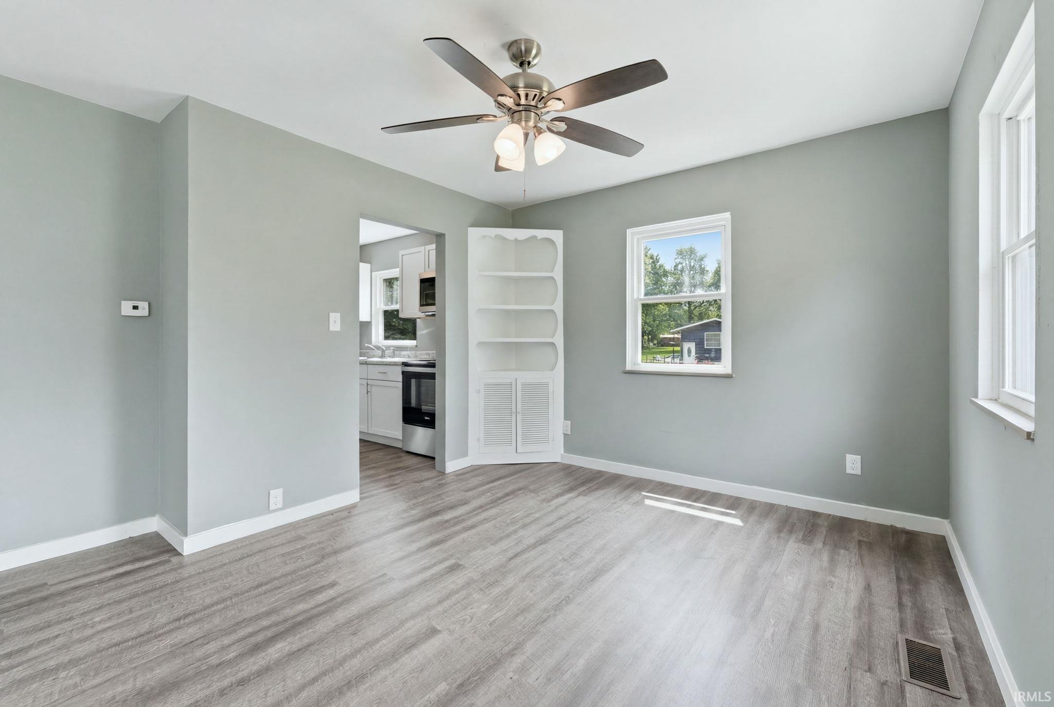 Spacious interior room featuring wood-finish flooring, a ceiling fan with light fixture, and a built-in corner shelving unit