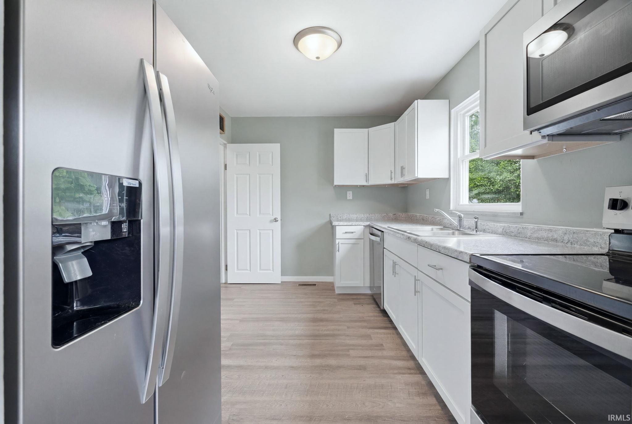 Bright kitchen featuring white cabinetry, stainless steel appliances, wood-finish flooring, a window above the sink, and light gray countertops