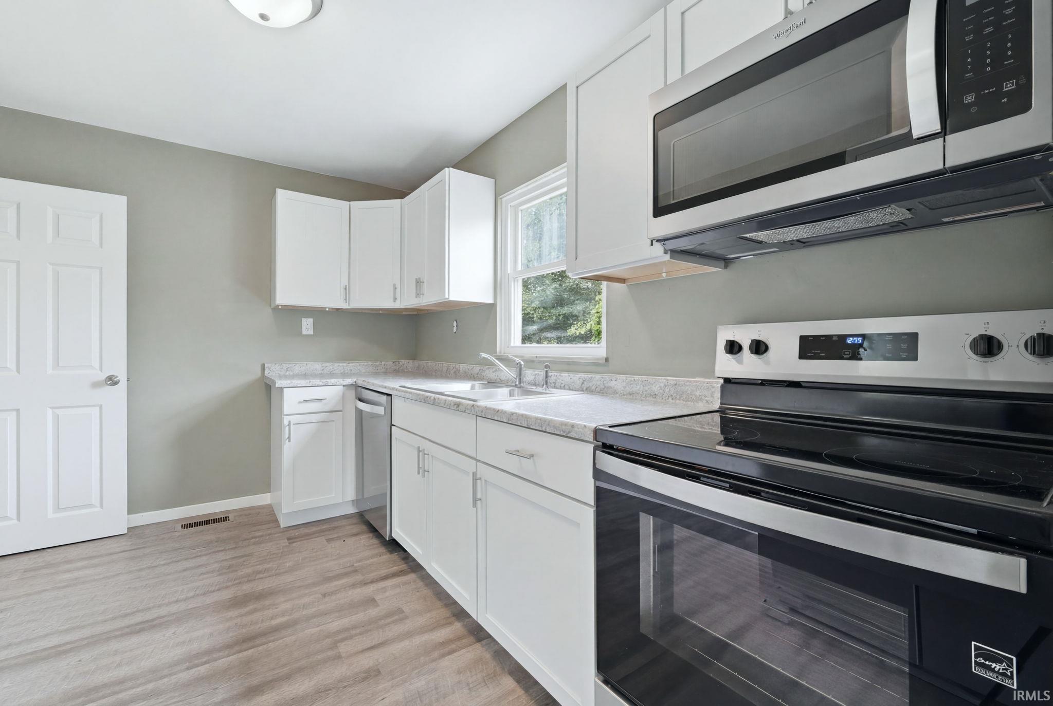 Modern kitchen featuring white cabinetry, light countertops, wood-finish flooring, a stainless steel microwave, and a black and stainless steel range