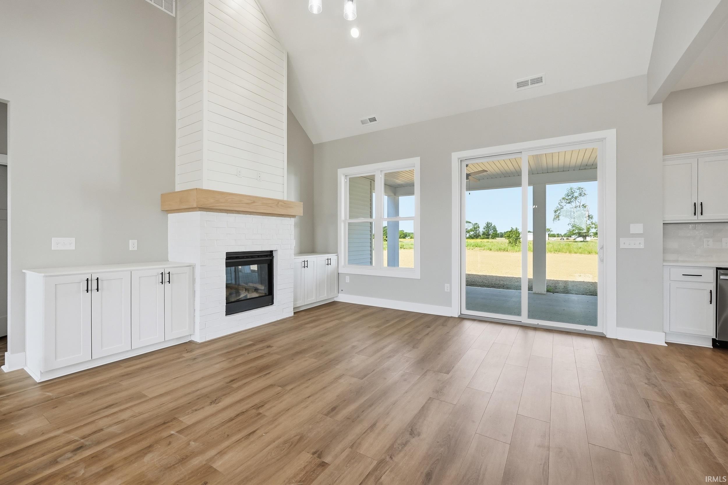 Spacious living area featuring vaulted ceilings, wood-finish flooring, and a floor-to-ceiling brick fireplace with a wood mantle