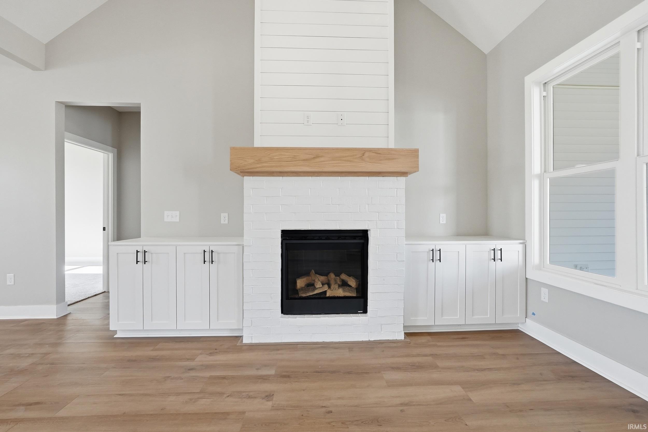Central fireplace featuring white brick surround, a natural wood-finish mantel, and a shiplap accent wall extending to the vaulted ceiling