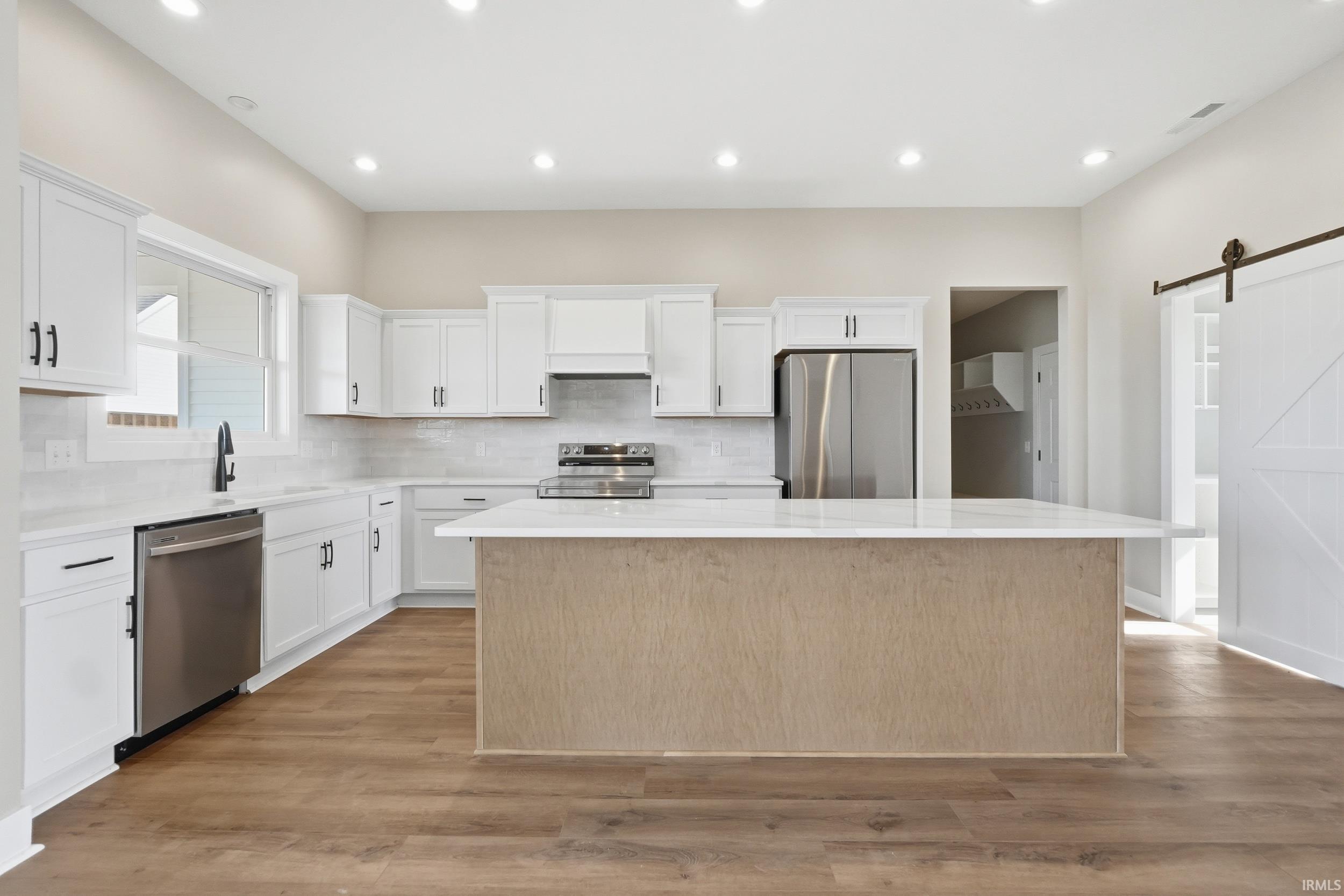 Expansive kitchen featuring a large central island with a light-toned base, white countertops, and wood-finish flooring