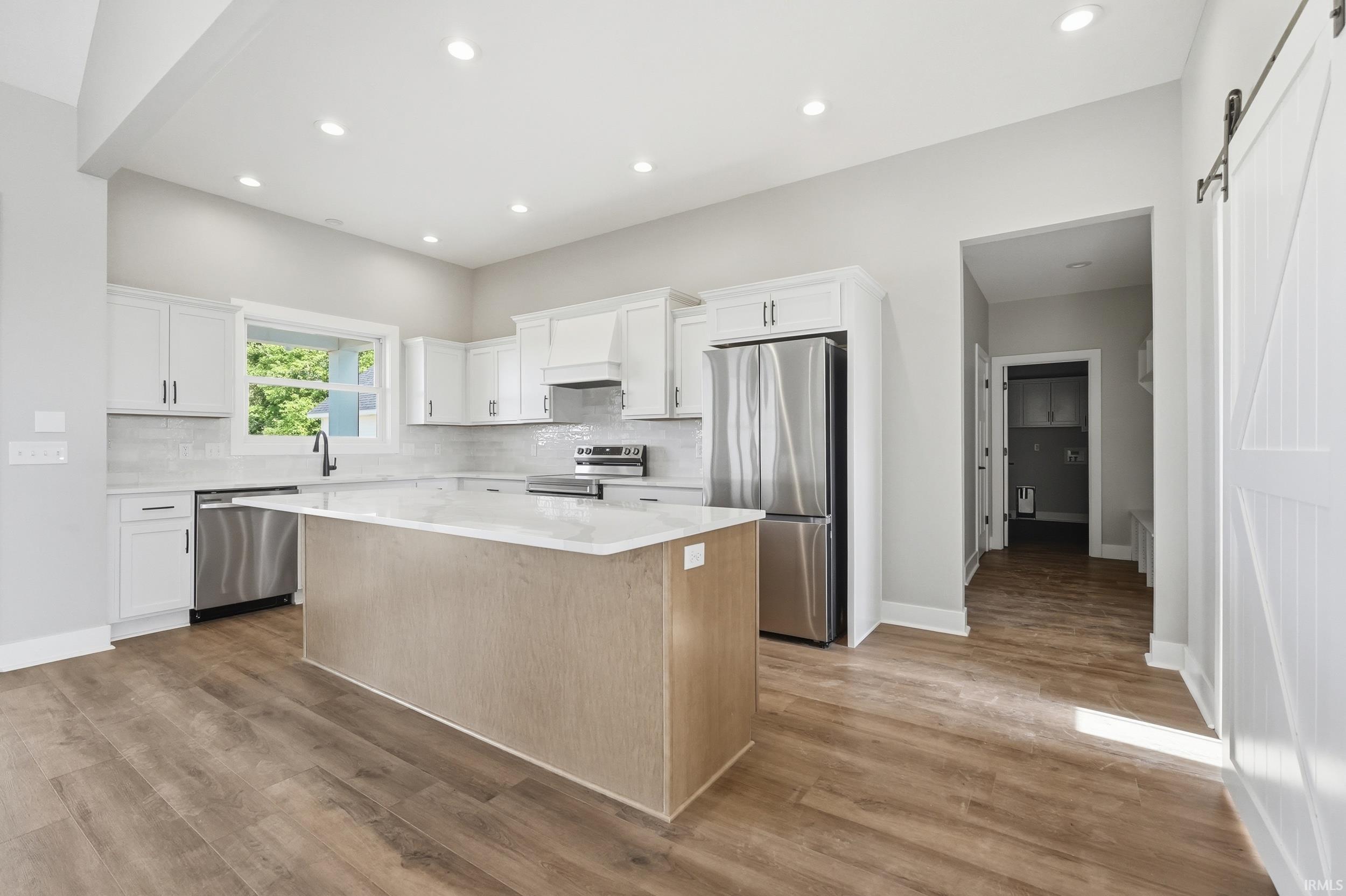 Modern kitchen featuring white cabinetry, stainless steel appliances, a center island with a light-colored countertop, recessed lighting, and wood-finish flooring