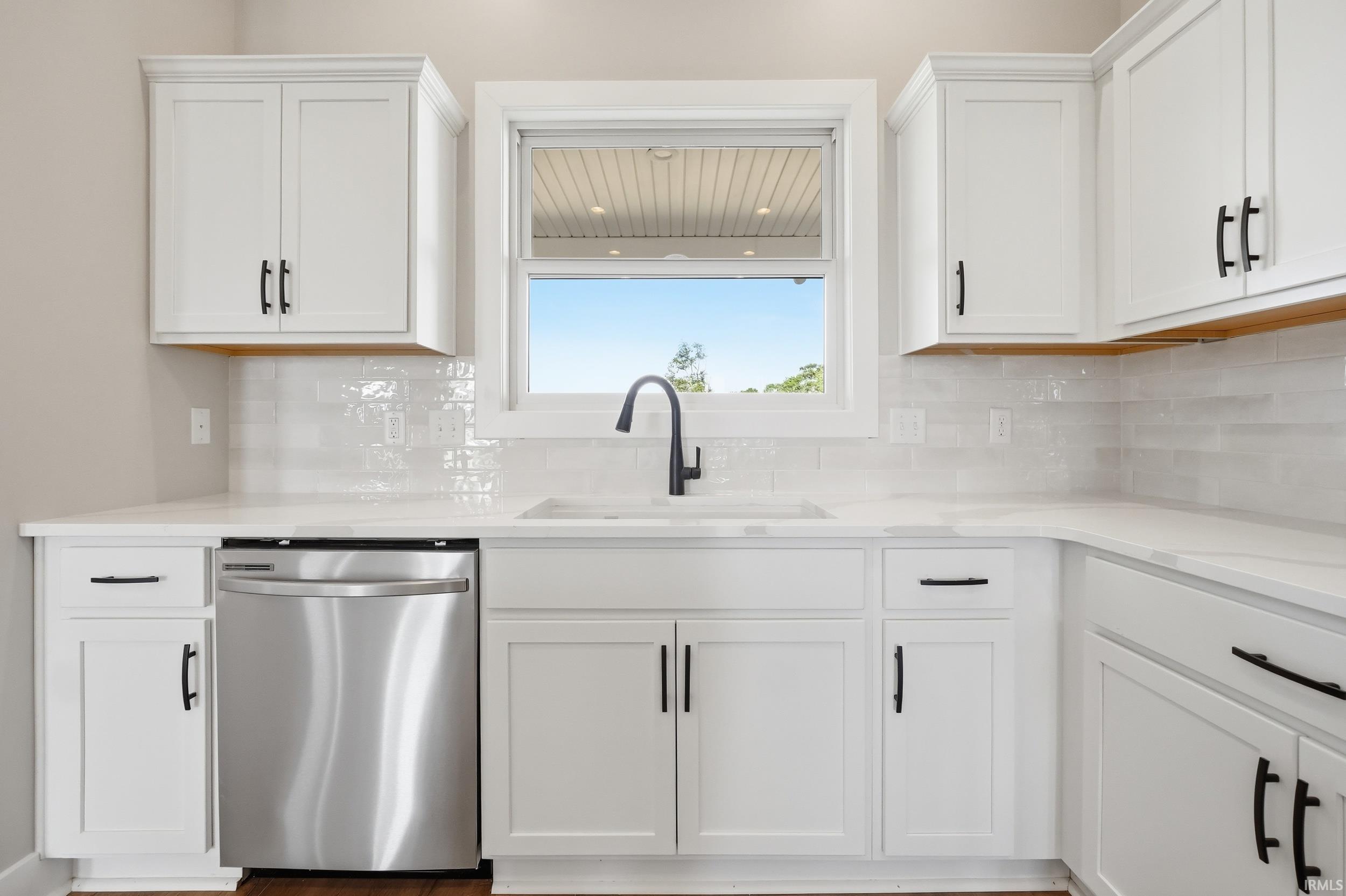 Kitchen featuring white shaker cabinetry with dark hardware, a stainless steel dishwasher, white countertops, and a white subway tile backsplash