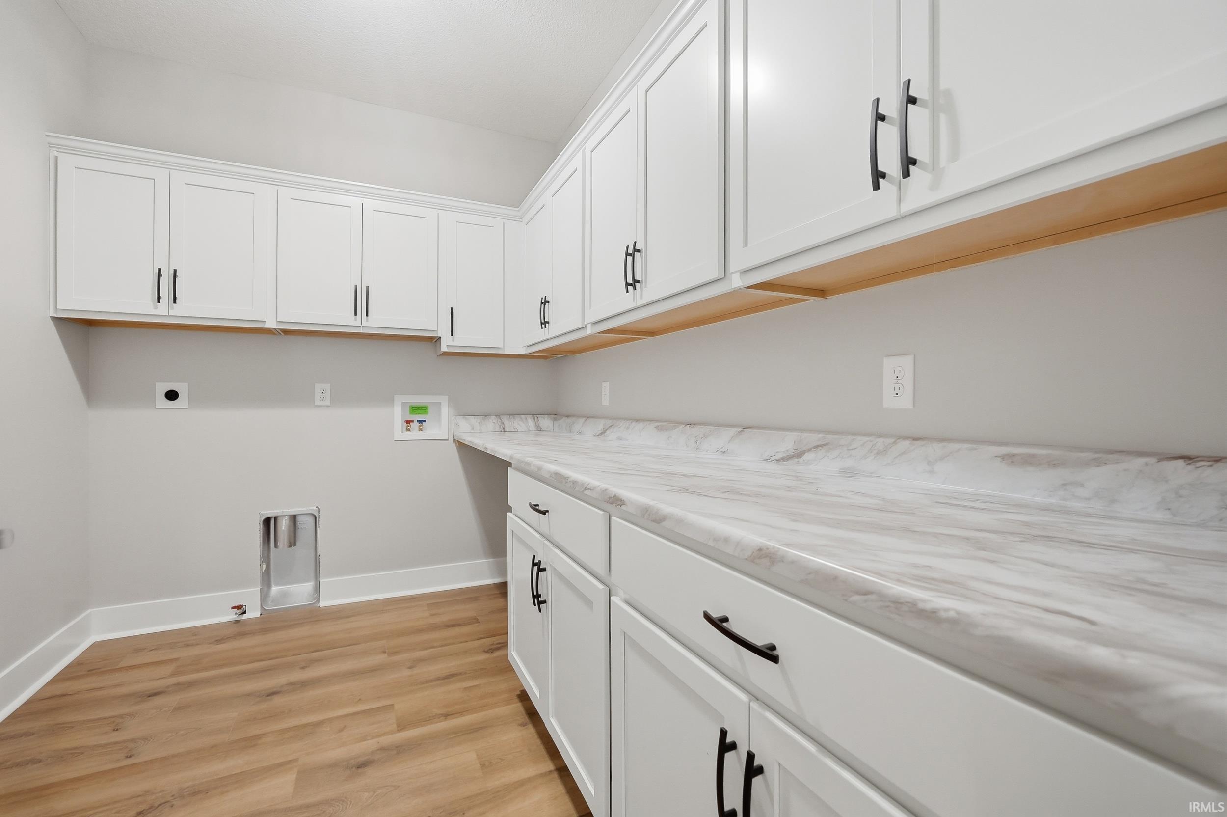 Laundry space featuring extensive white cabinetry with matte black hardware, wood-finish flooring, and a marble-look countertop