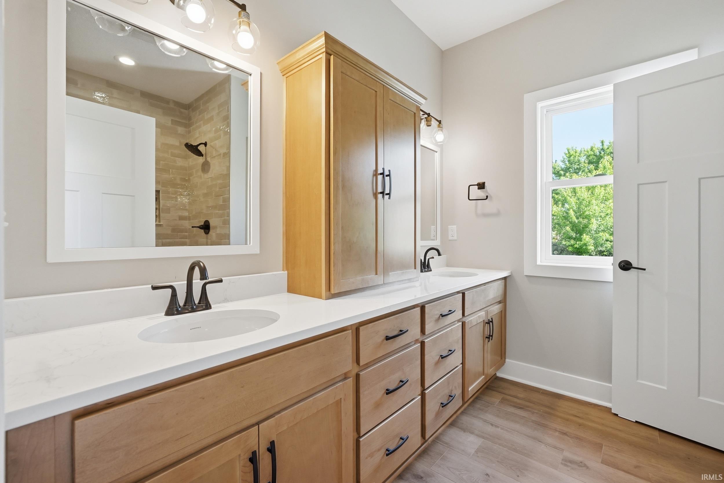 Dual vanity with white countertops, light wood-finish cabinetry, and matte black fixtures