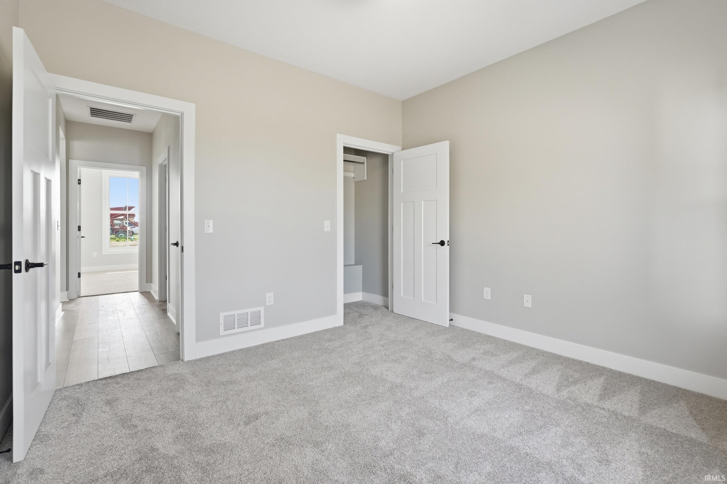 Carpeted room with a neutral wall palette, white trim, and a white interior door with black hardware
