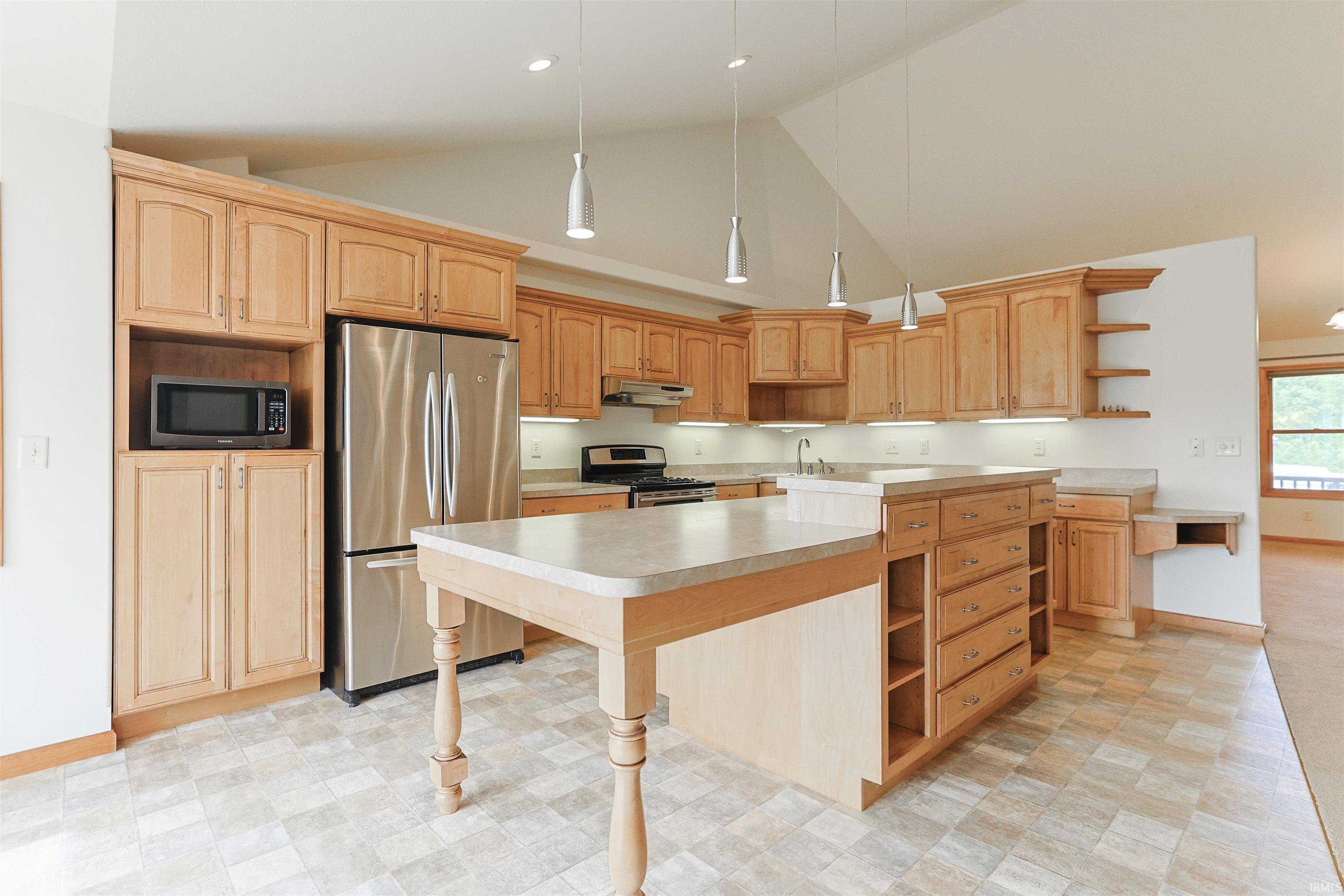Kitchen featuring a vaulted ceiling with pendant lighting, wood cabinetry, stainless steel appliances, and a central island with a built-in cooktop
