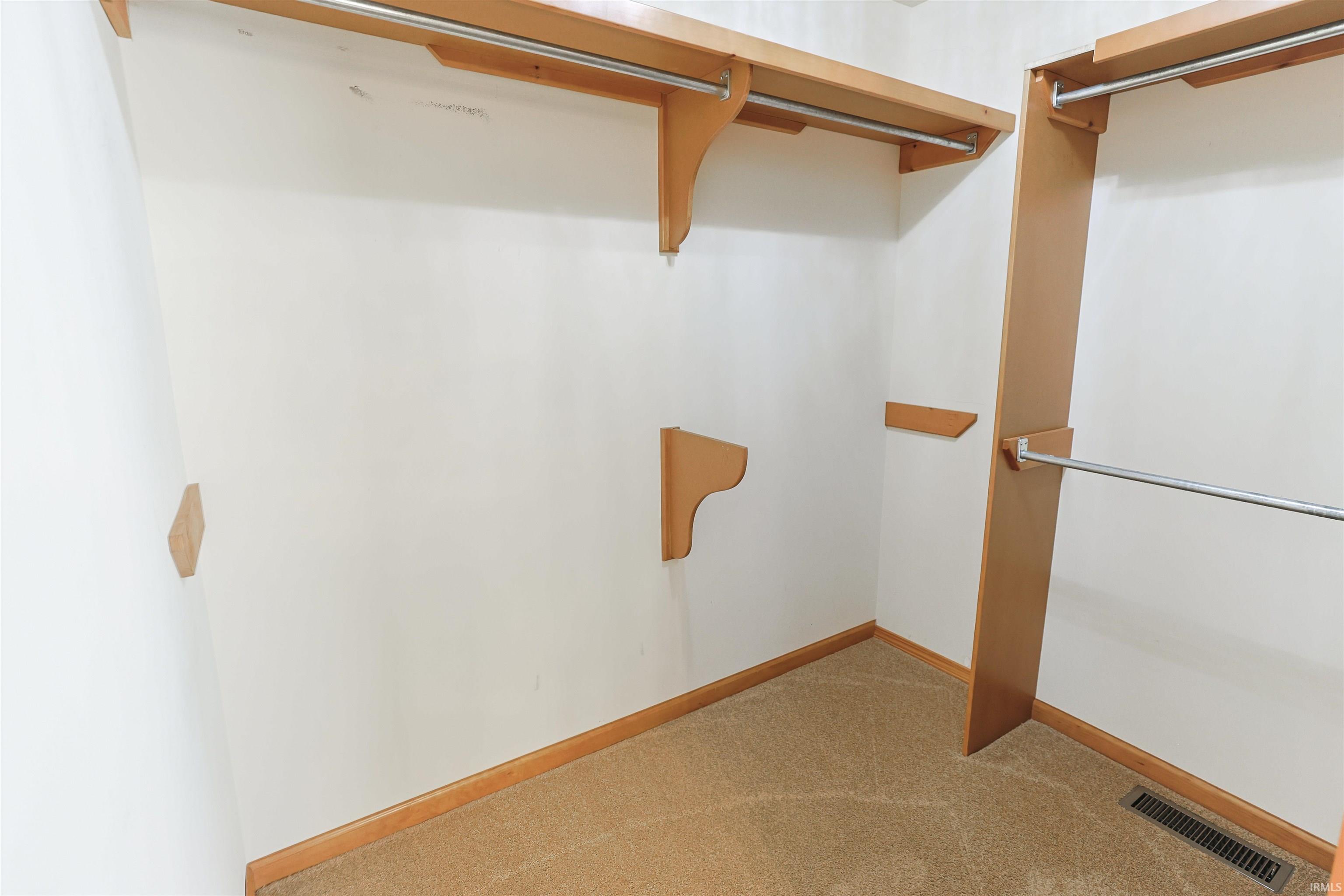Walk-in closet featuring light wood-finish shelving, chrome hanging rods, and carpet flooring