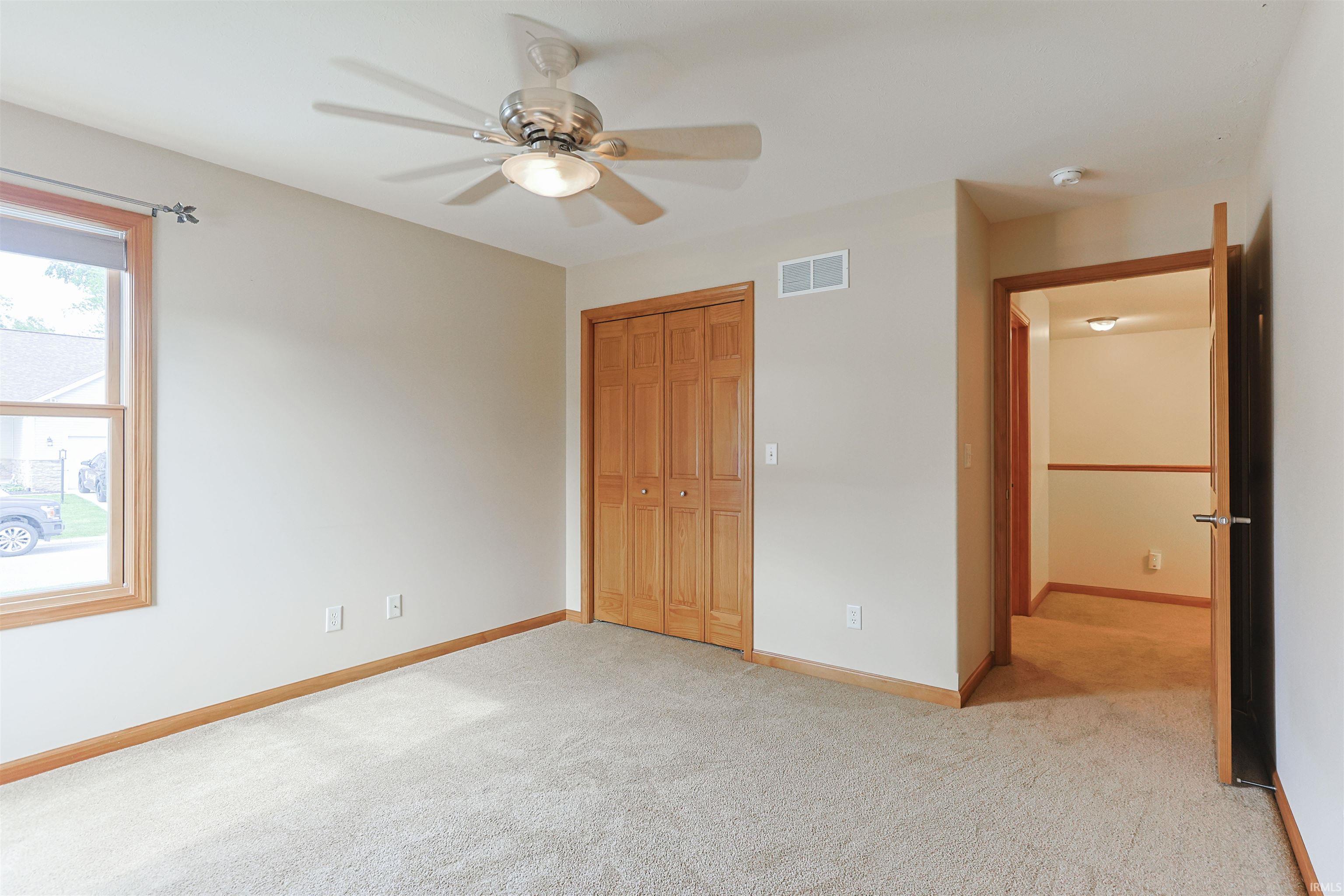 Neutral-toned carpeting, a ceiling fan with integrated lighting, and natural wood bi-fold closet doors