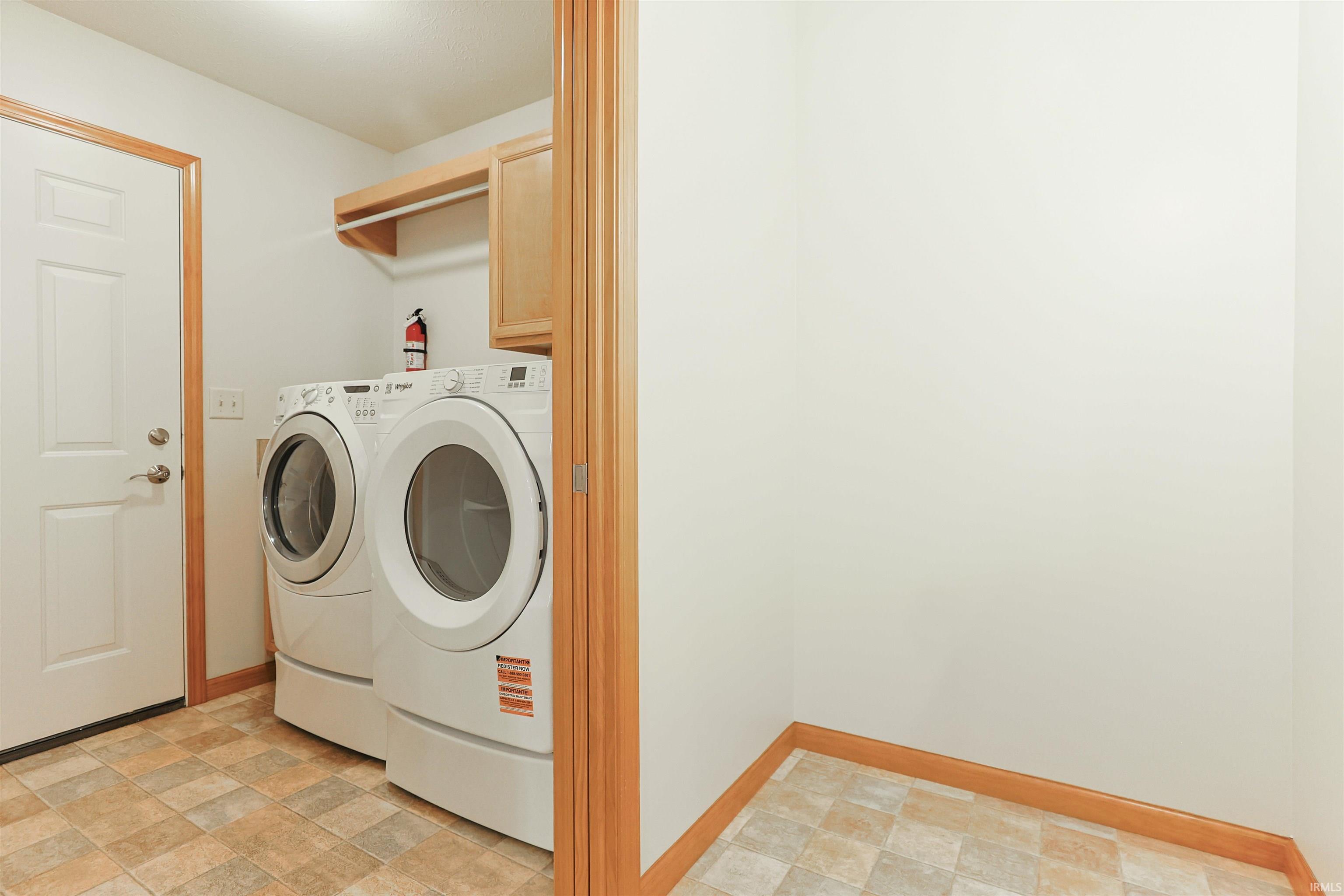 Dedicated laundry area featuring tile flooring, light wood trim, a built-in upper cabinet, and an open storage shelf