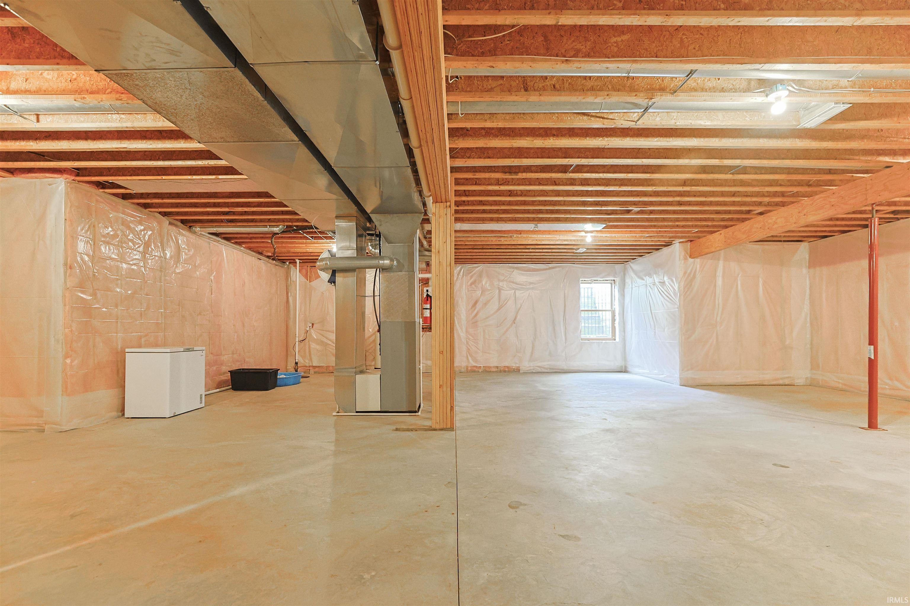 Unfinished basement featuring a concrete floor, exposed wood joists, two egress windows, and extensive open space