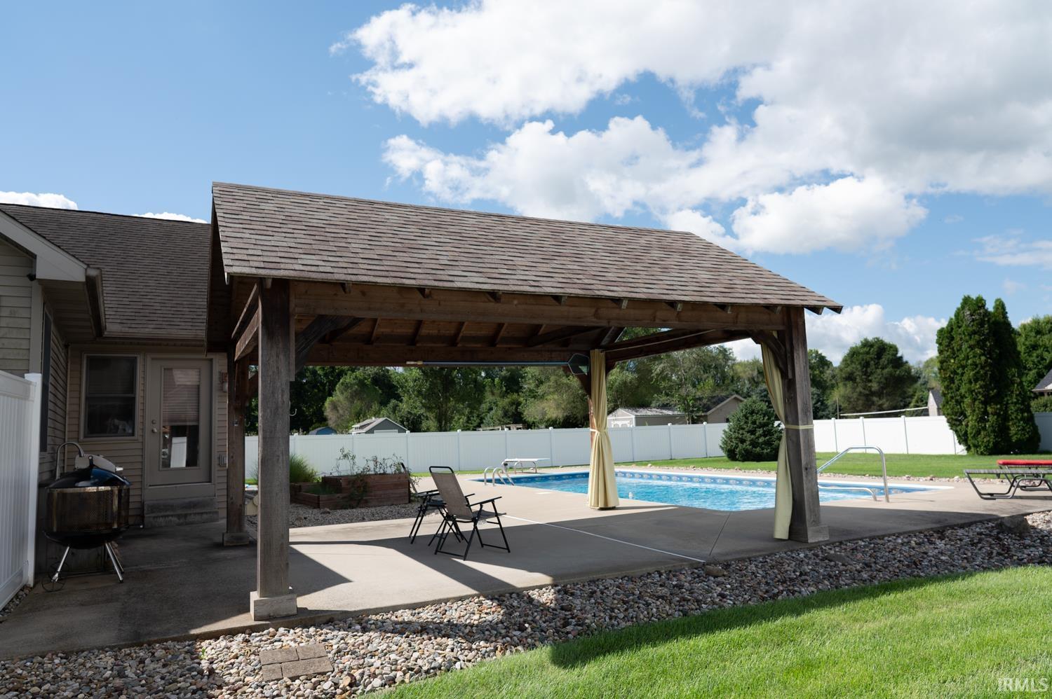Outdoor entertainment area featuring a covered patio with a shingle roof, concrete decking, and a fenced in-ground swimming pool