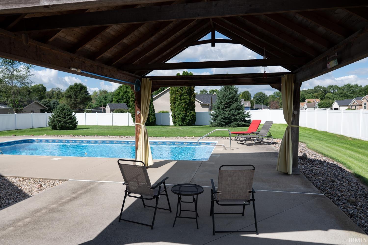 Covered patio with a high vaulted wood-finish ceiling, overlooking a swimming pool with a concrete surround