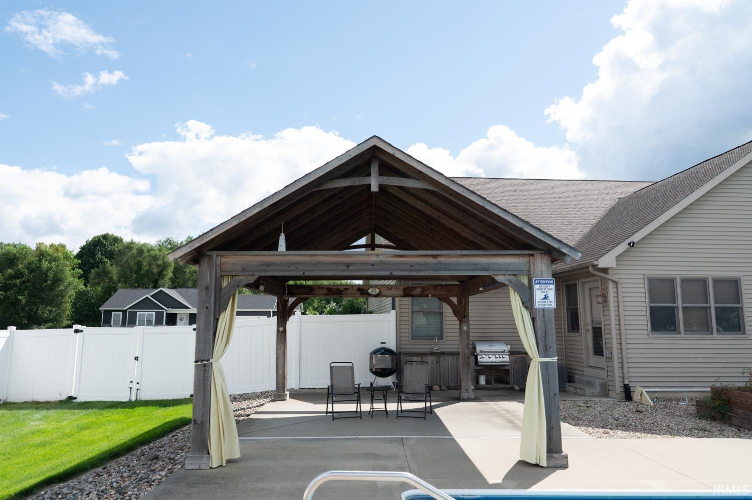 Outdoor covered patio featuring a gabled wood-frame roof, concrete flooring, and privacy curtains