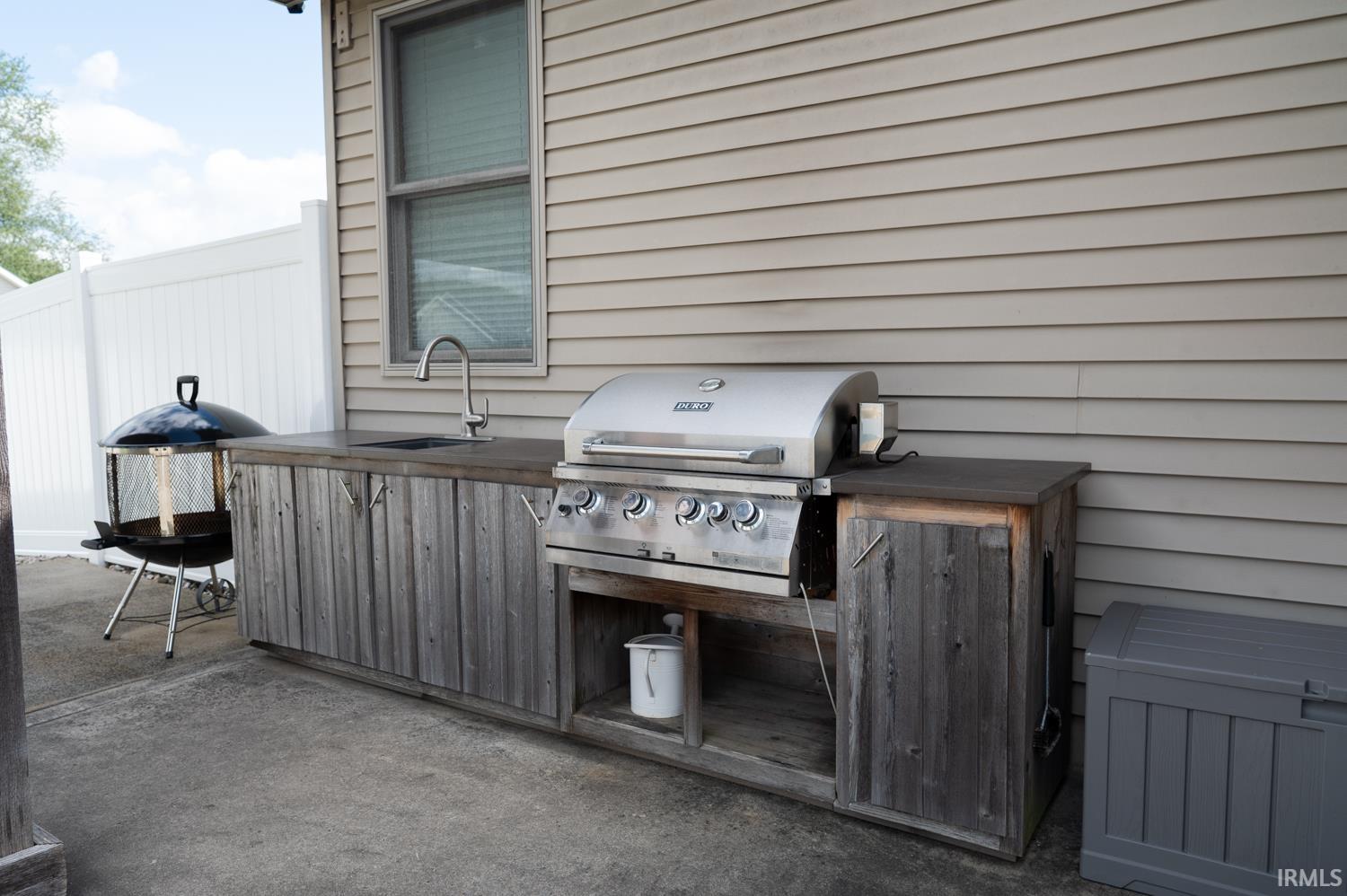 Outdoor kitchen featuring an integrated sink with a gooseneck faucet, an under-mount grill, and a wood-finish cabinet base with built-in storage