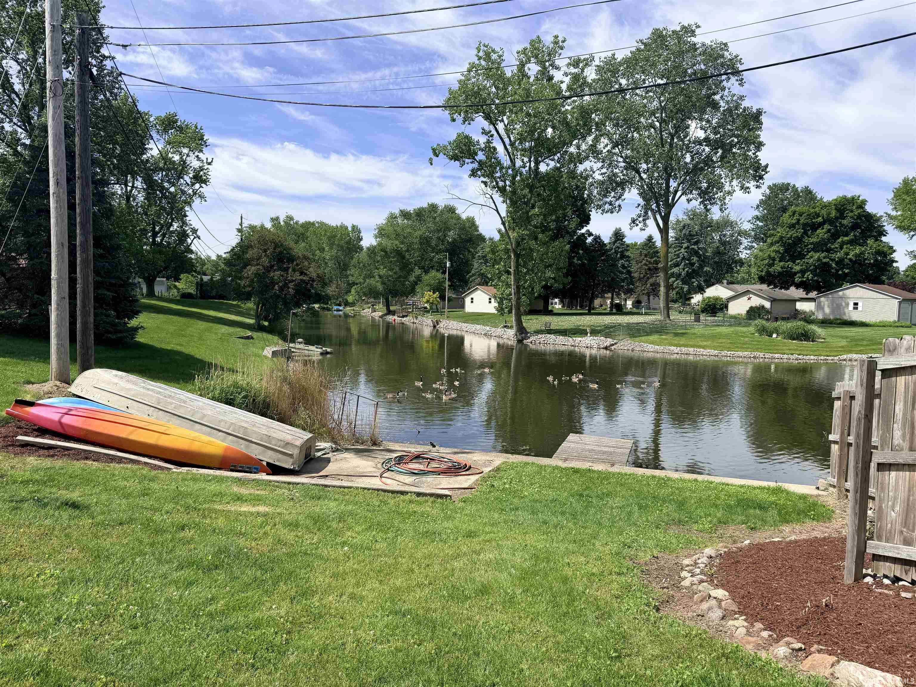 Waterfront backyard with a wooden fence, boat launch, and mature trees