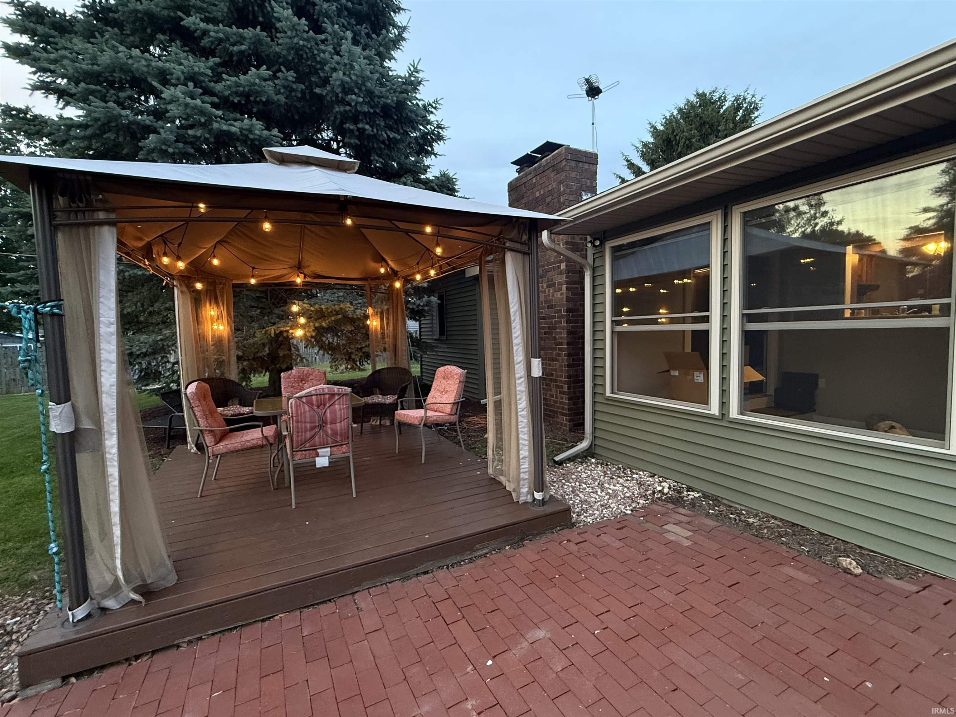 Outdoor entertaining area featuring a dark wood-finish deck with a covered gazebo, illuminated by string lighting