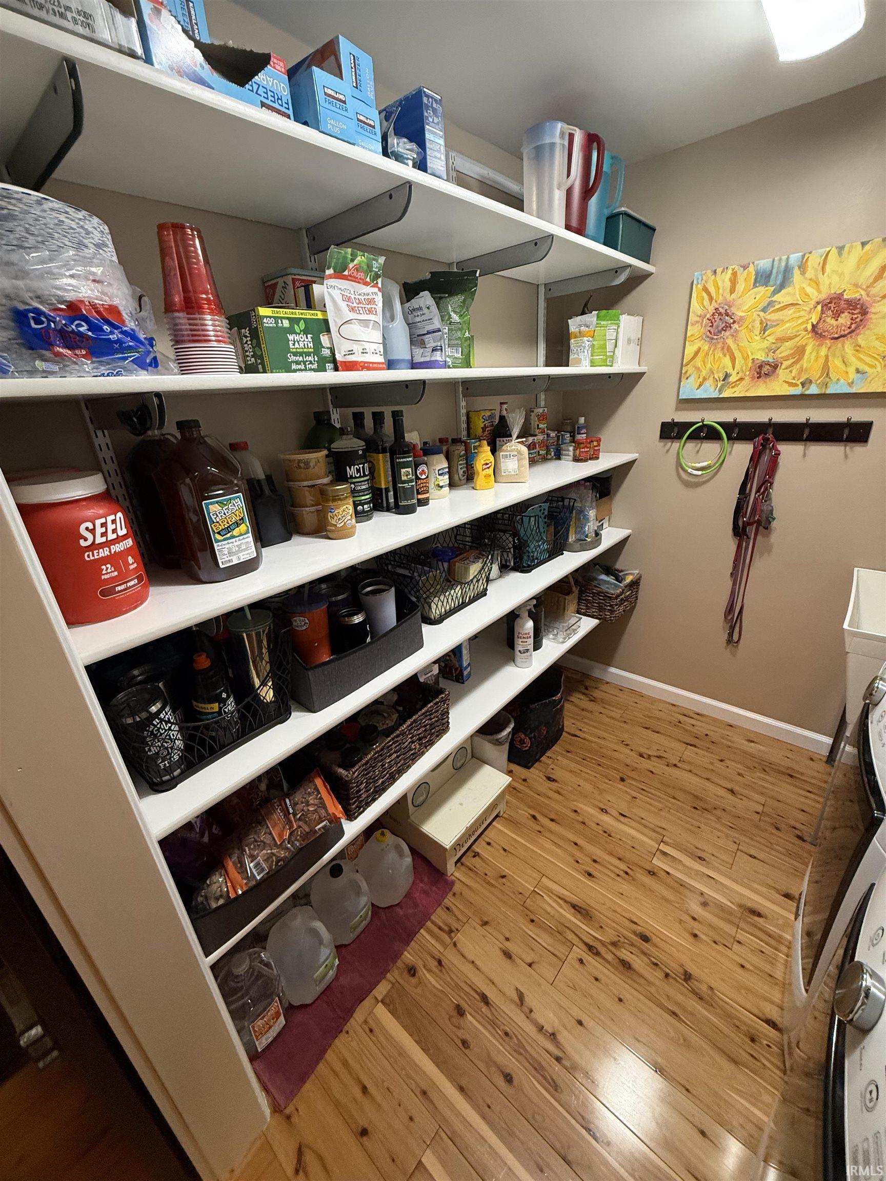 Built-in shelving system with adjustable white shelves, light-toned wood-finish flooring, neutral wall paint, and a wall-mounted hook rack