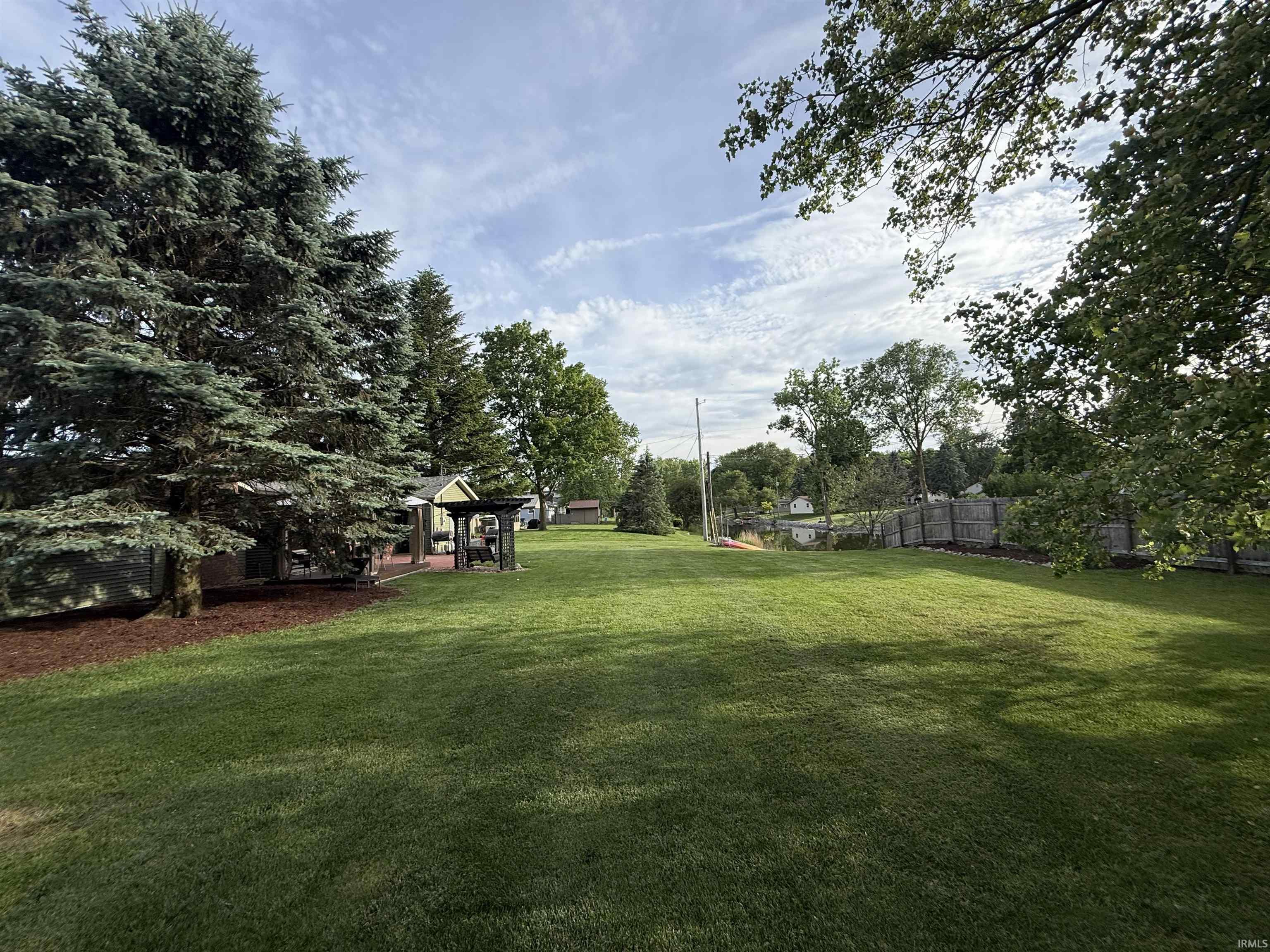 Expansive grassy yard featuring mature evergreen trees and a dedicated outdoor entertainment area with a pergola